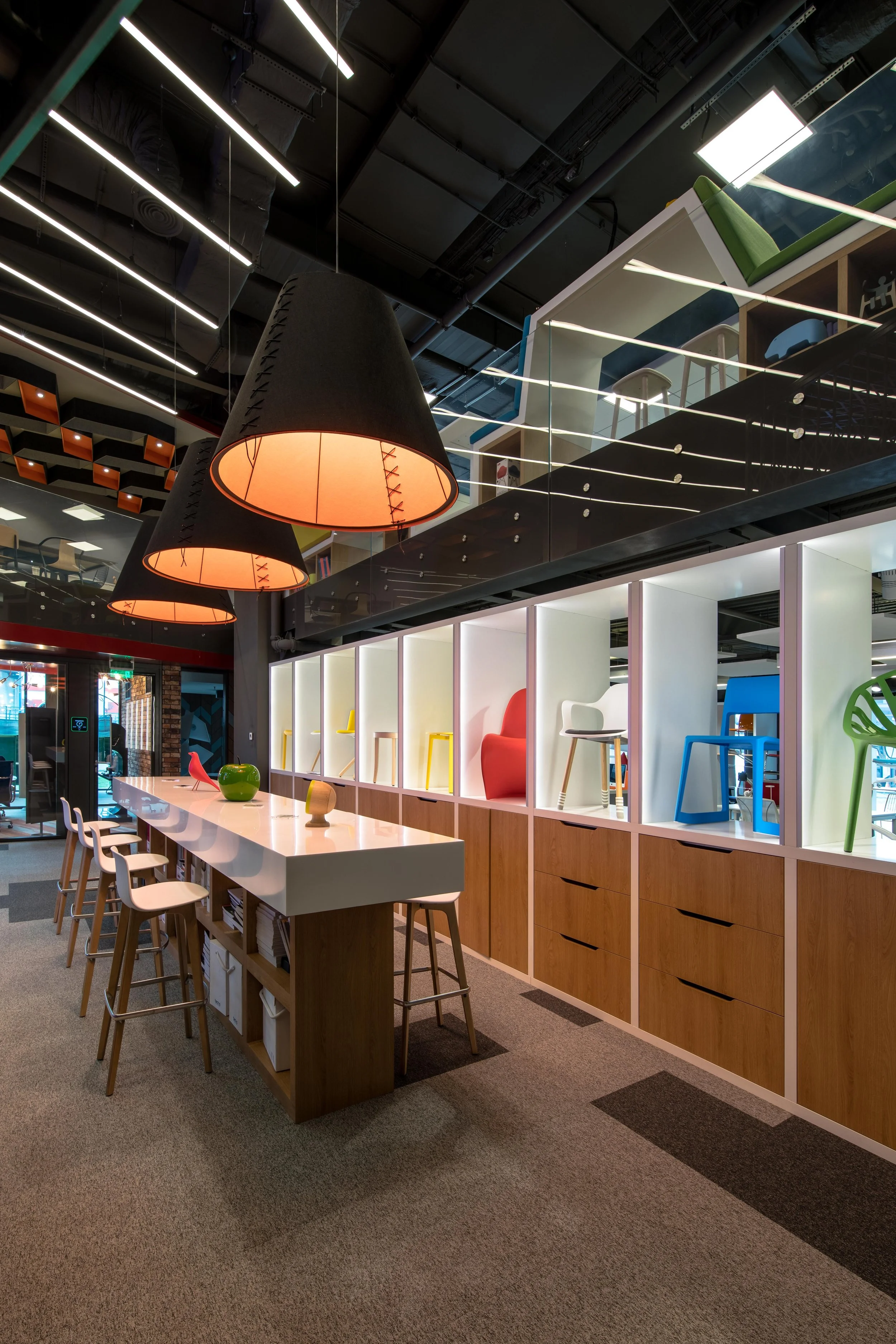 Modern furniture store display with chairs, stools, and chairs on shelves, pendant lights, and a long white table with decorative objects.
