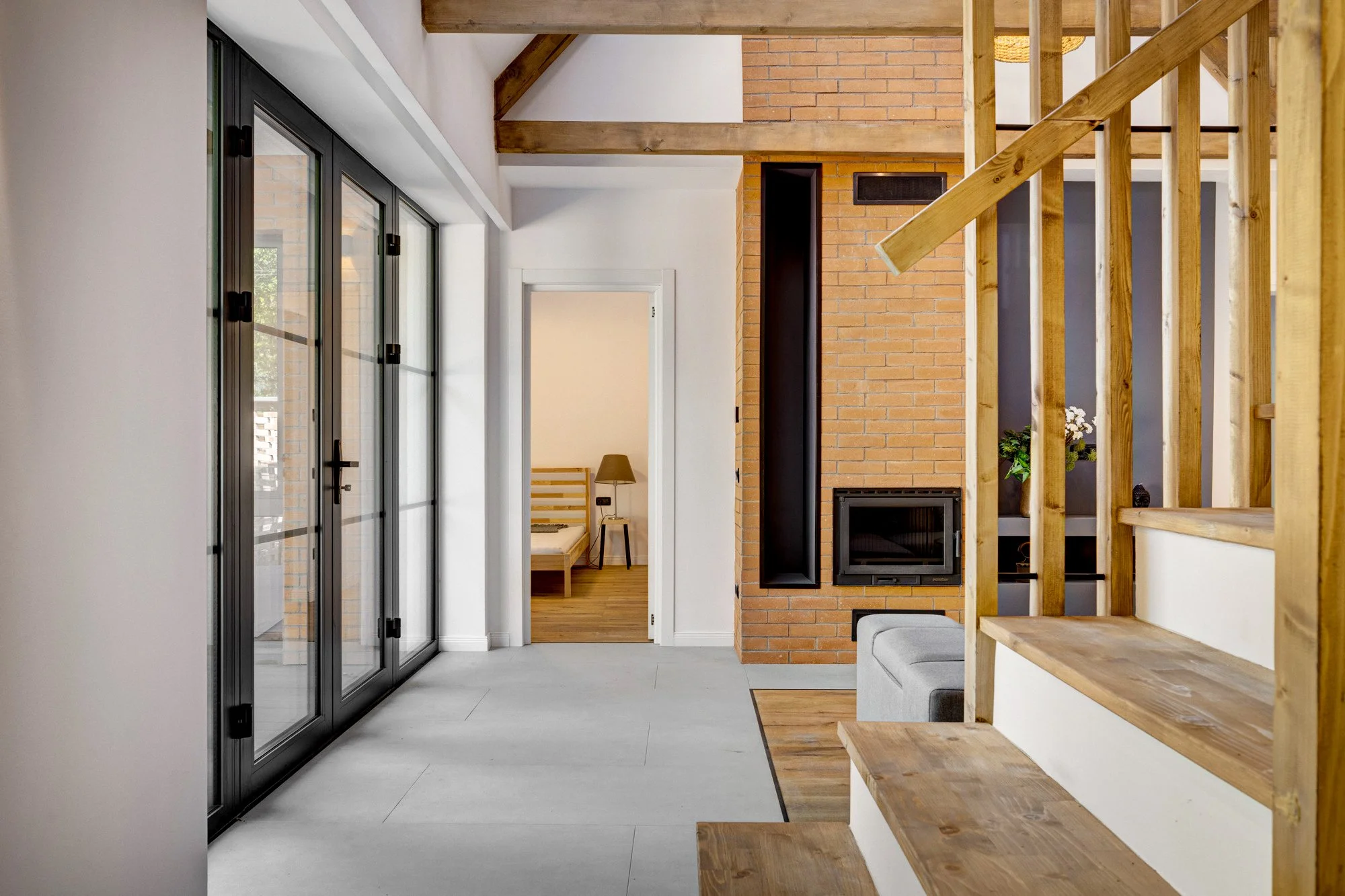 Modern living space with large glass sliding doors, a brick fireplace, and wooden stairs.