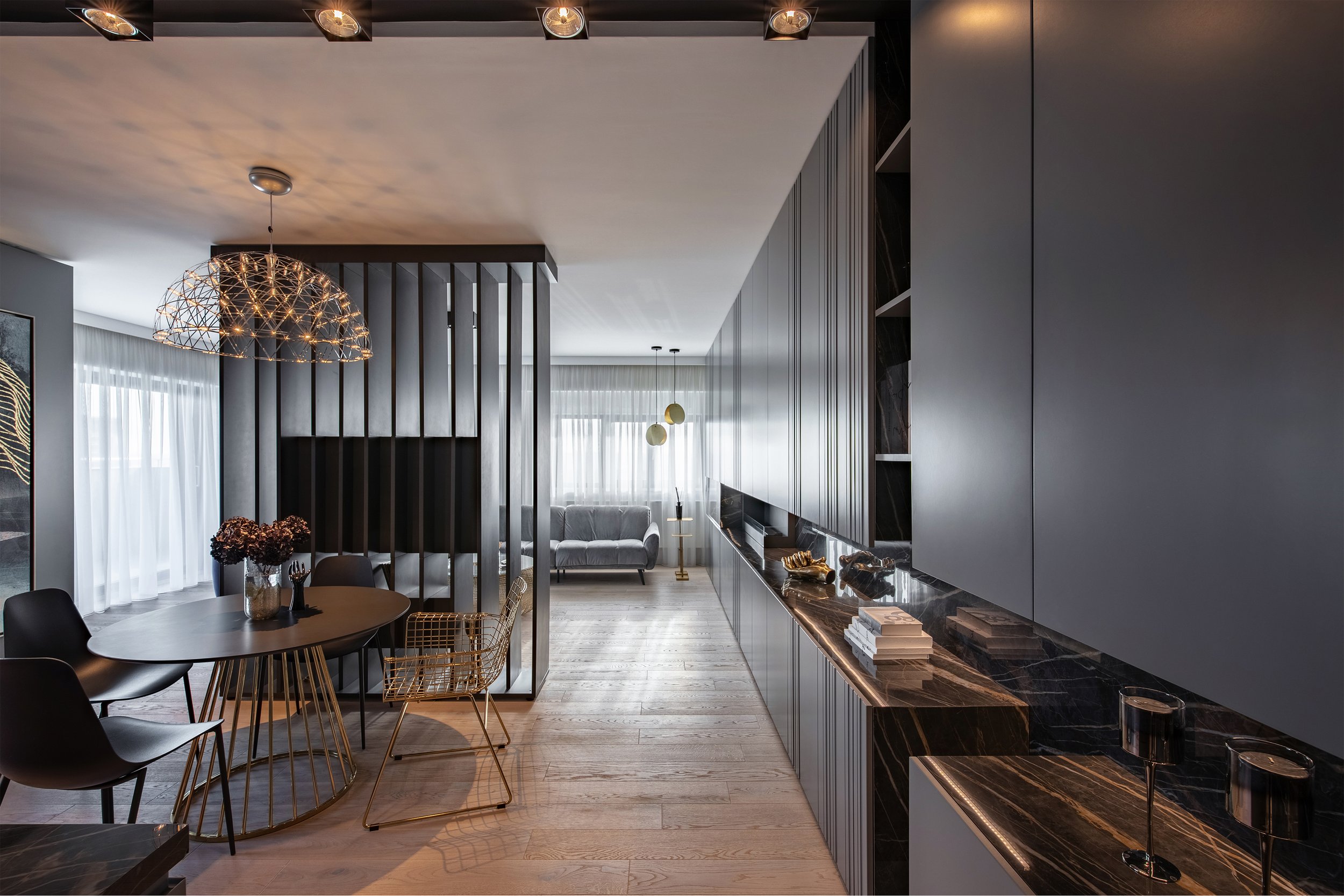Modern living room and dining area with black and gray decor, wooden flooring, and large windows with sheer curtains.