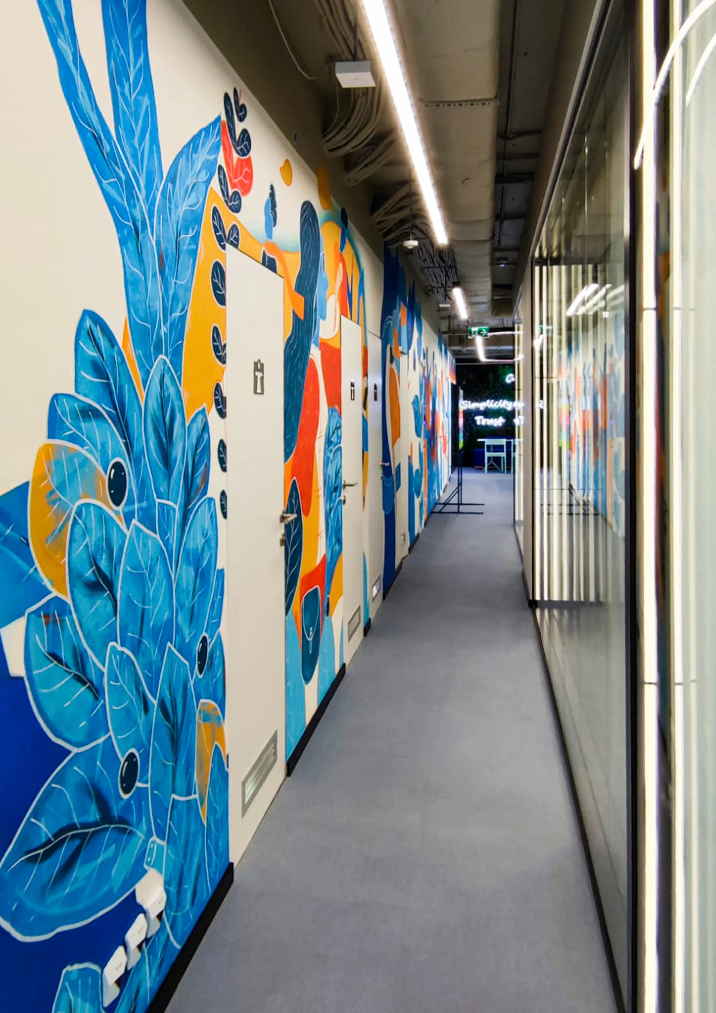 Colorful mural with plants and abstract shapes on a hallway wall.