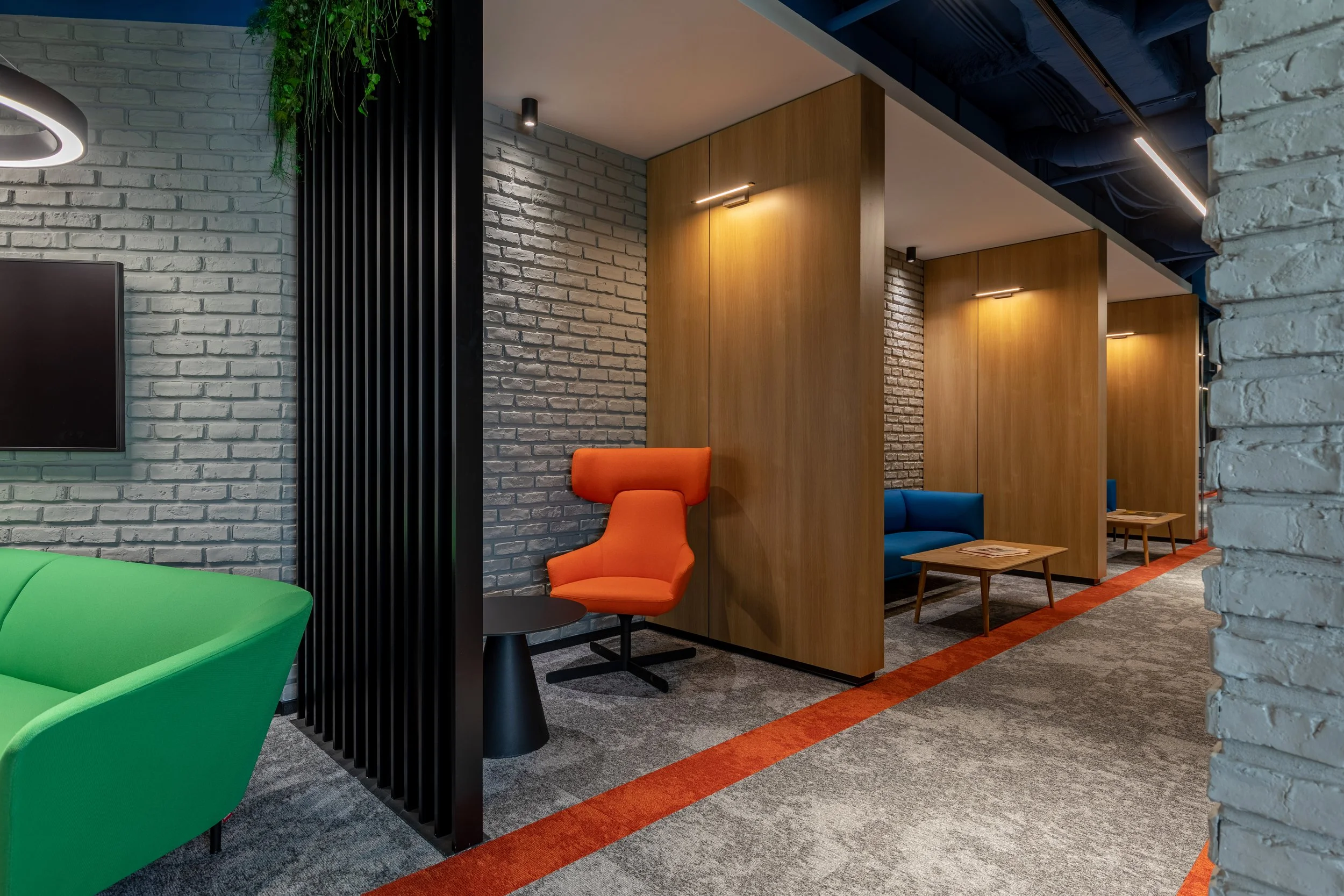 Modern lounge area with colorful chairs, gray brick walls, wooden partitions, and a gray and orange carpet.