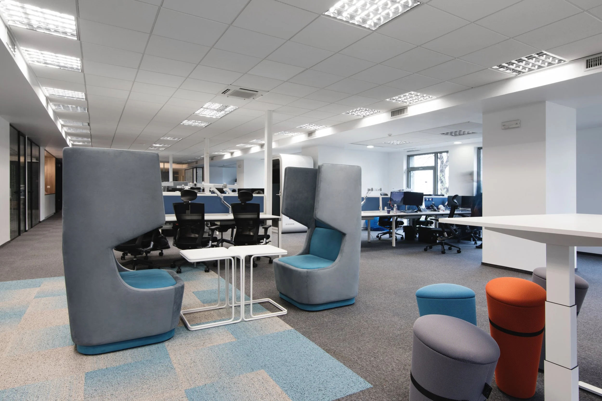 Modern open-plan office with high-backed chairs, tables, computer desks, and windows.