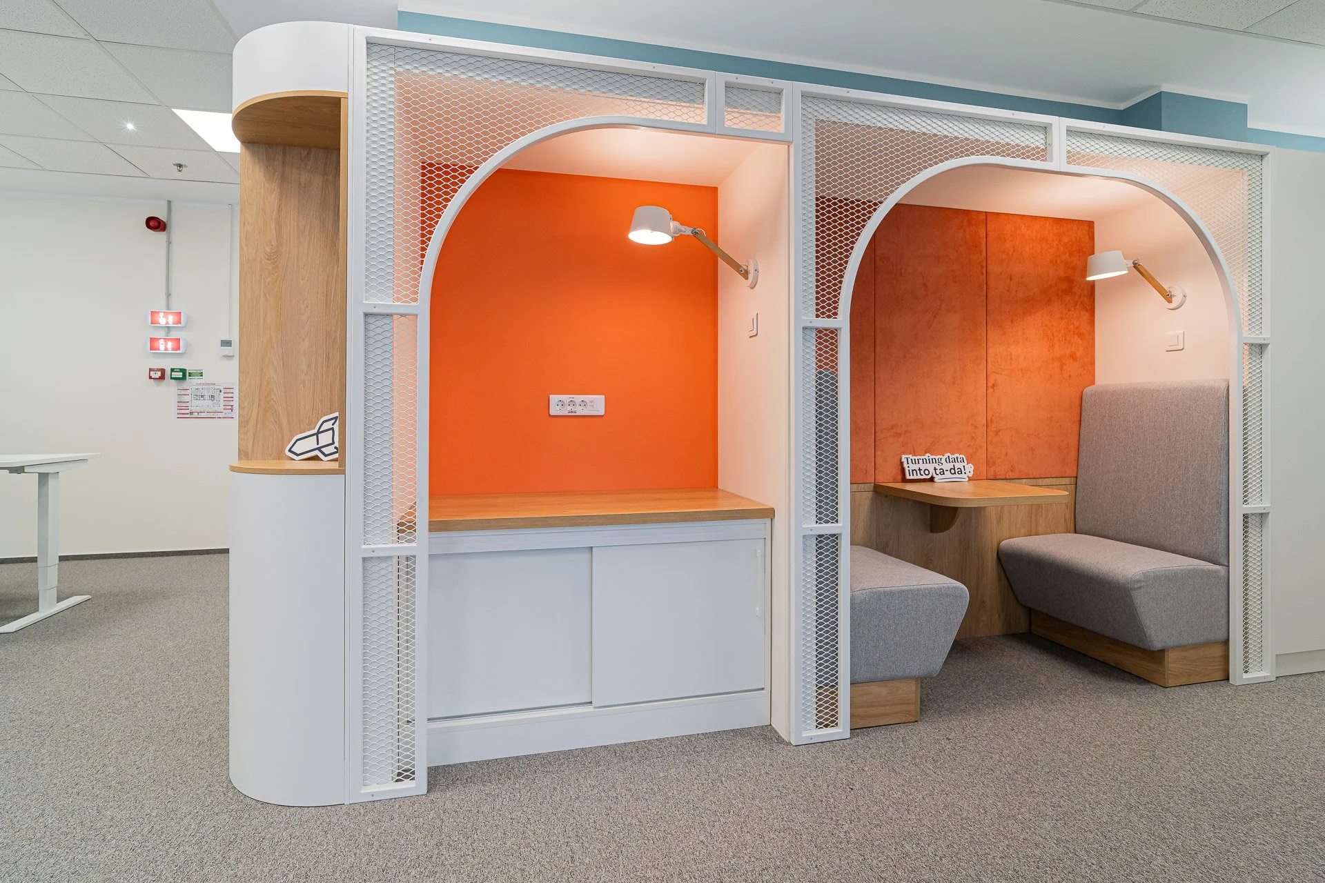 Two adjacent semi-private seating areas with curved arches, orange and gray wall backgrounds, wall-mounted lights, and wooden tabletops. The area on the right has a sign that says "Turning data into ta-da!".