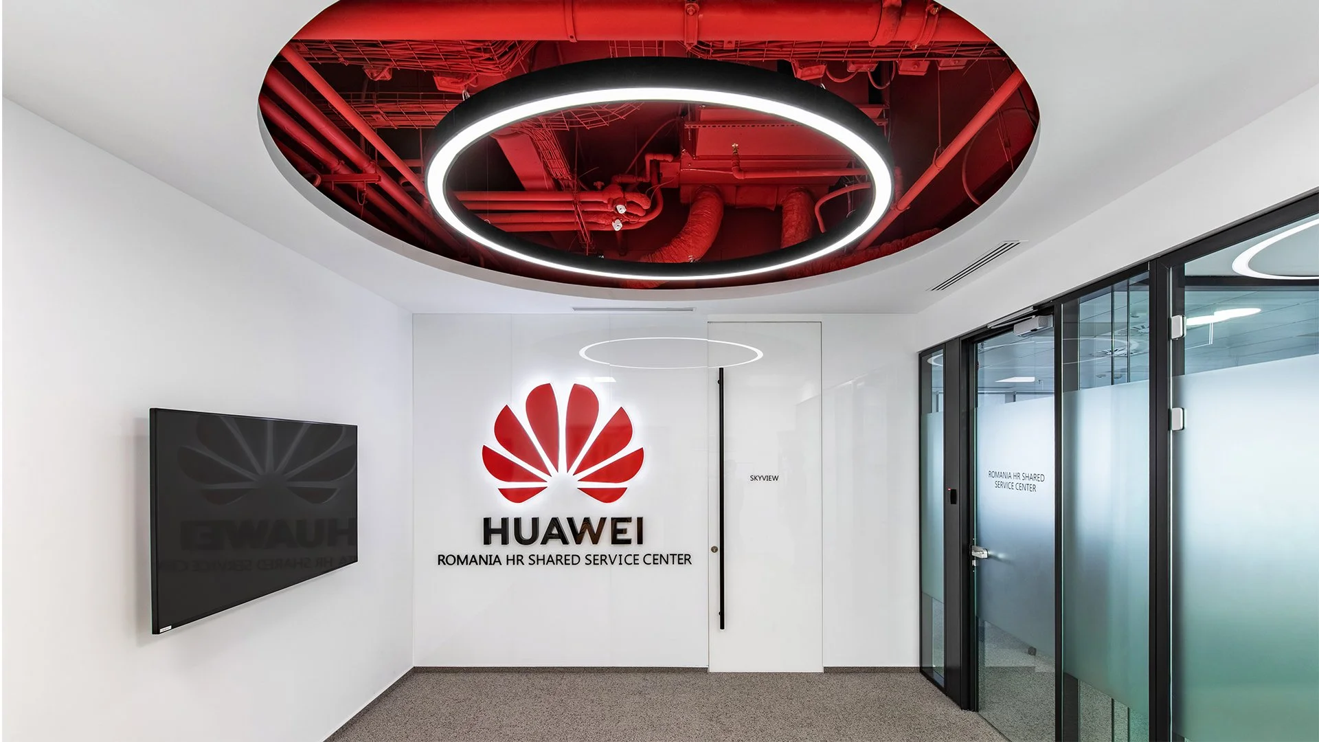 Entrance to Huawei Romania HR shared service center with large Huawei logo on the wall, glass doors, and modern circular ceiling lights