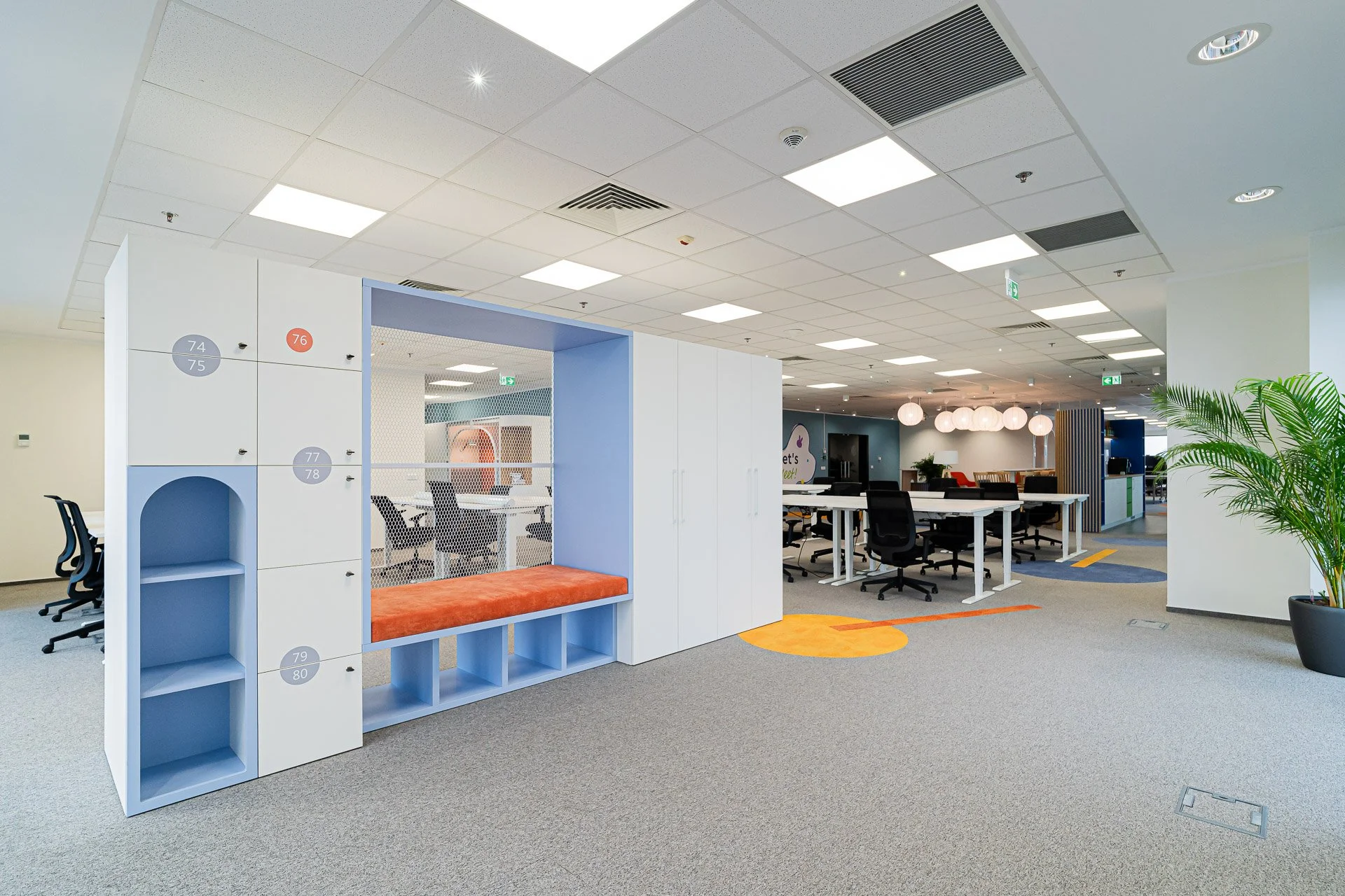 Open office space with workstations, seating areas, and decorative lighting in a modern, brightly lit environment.