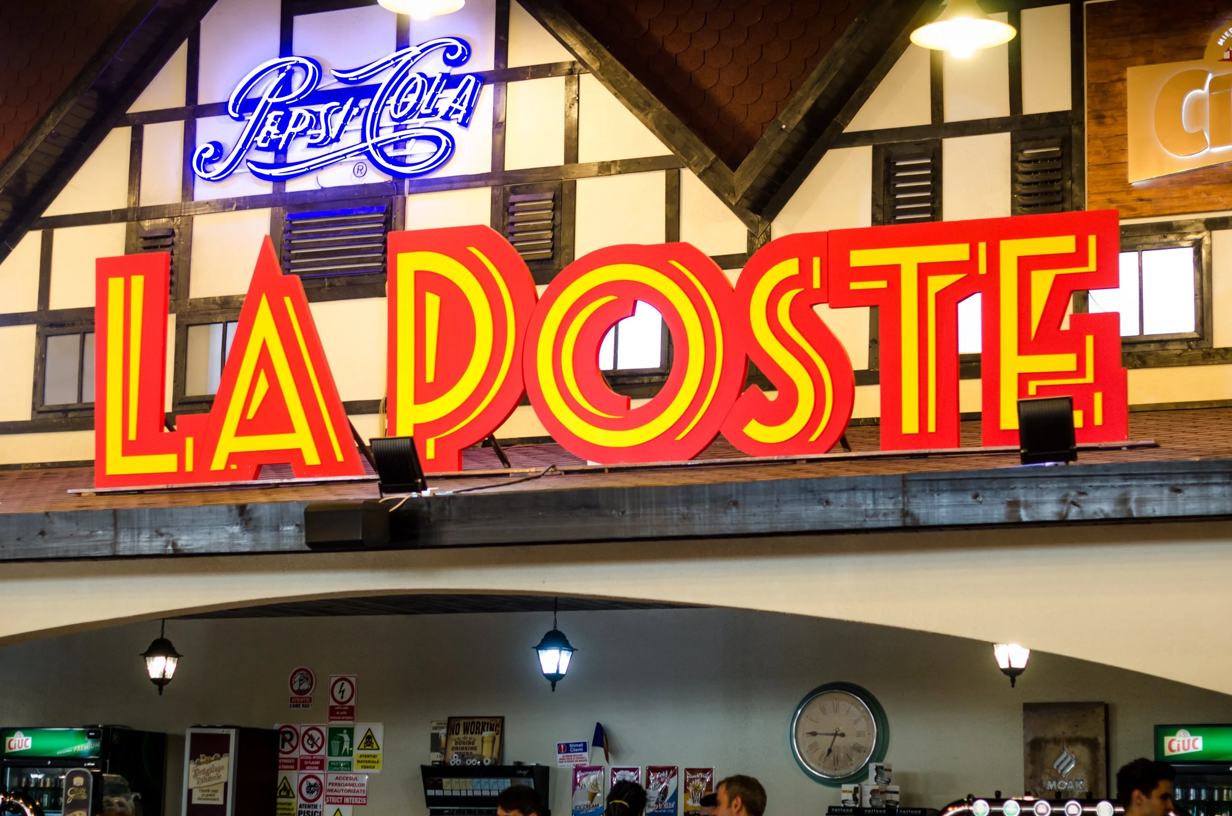 Bright neon sign reading 'LADOST' in red and yellow, with smaller blue neon sign reading 'Tepsi Torta' above it, inside a restaurant or cafe.