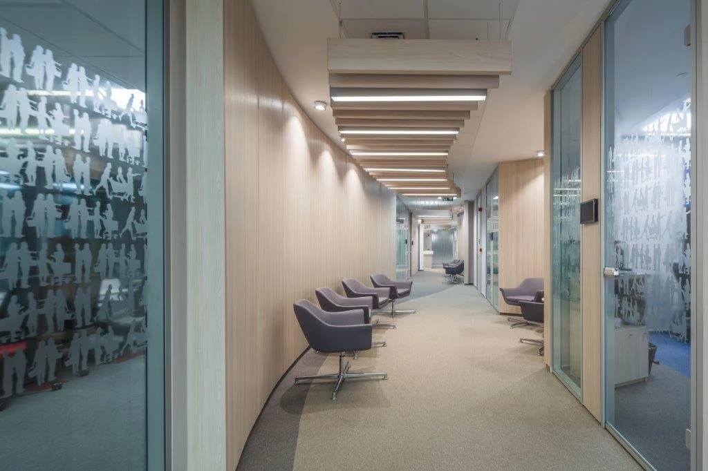 Modern office hallway with glass walls and gray armchairs along the walls.