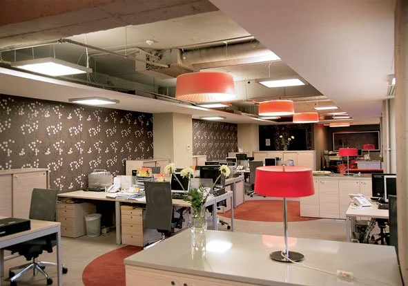 Office space with desks, chairs, computers, and decorative red lampshades hanging from the ceiling.