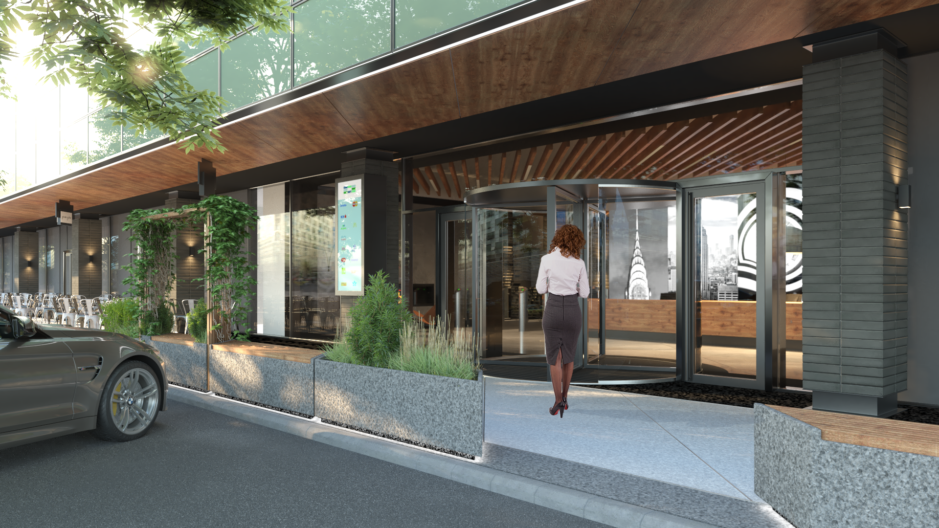 A woman in business attire walking into a modern building with a glass revolving door. The building has outdoor seating and lush greenery.