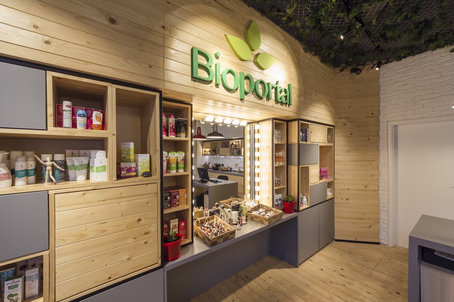 Interior of a wellness or beauty shop with wood storage units, grooming products, and a mirror with light bulbs, featuring a green 'Bioportal' sign on a wooden wall.