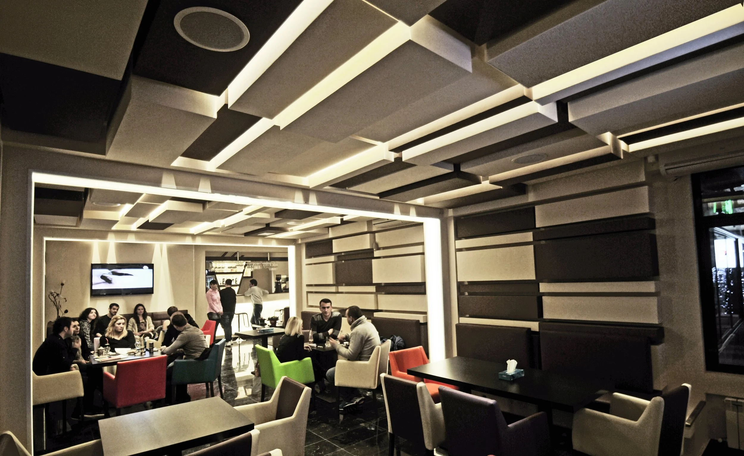 A modern restaurant interior with people dining at tables, a bar area in the background, and decorative wall panels.