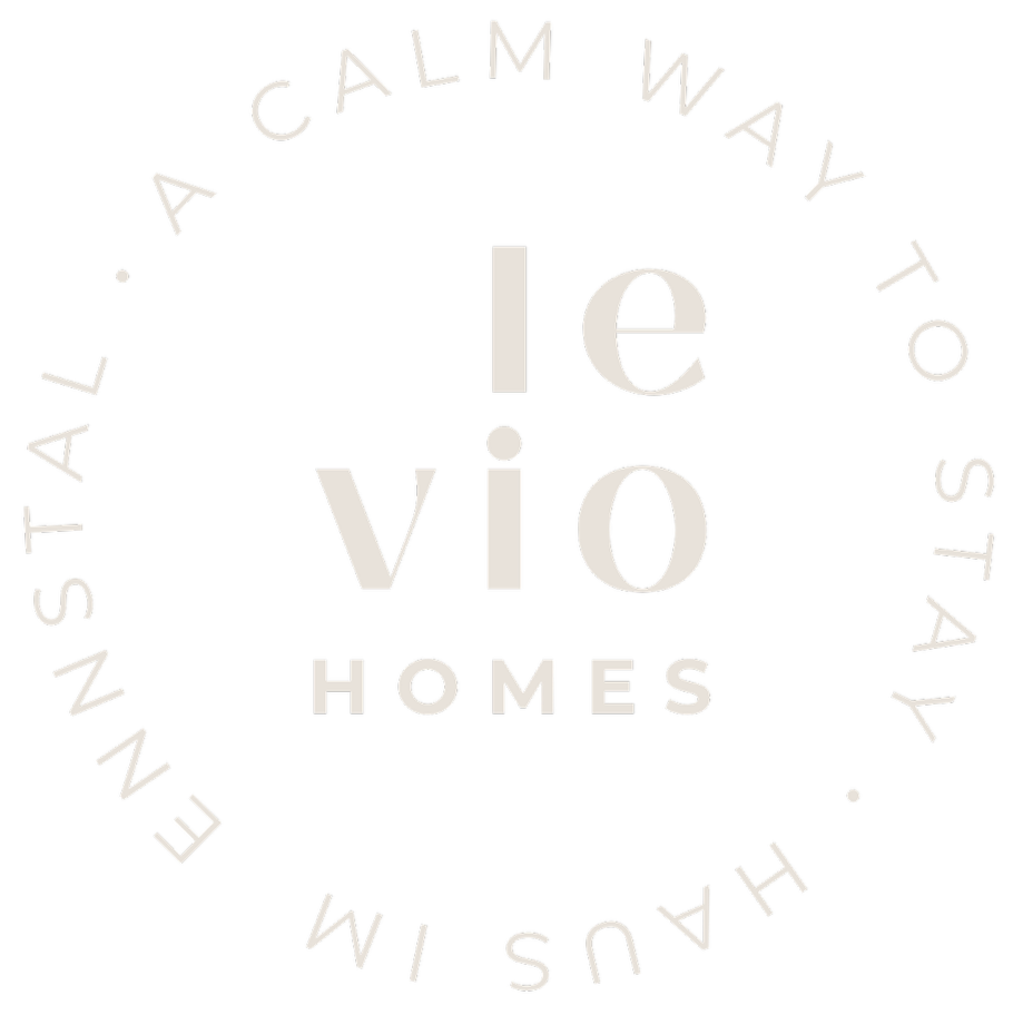 Der Schriftzug 'levio HOMES' umgeben von einem Kreis mit dem Text 'A CALM WAY TO STAY INNEST' gegen schwarzen Hintergrund.