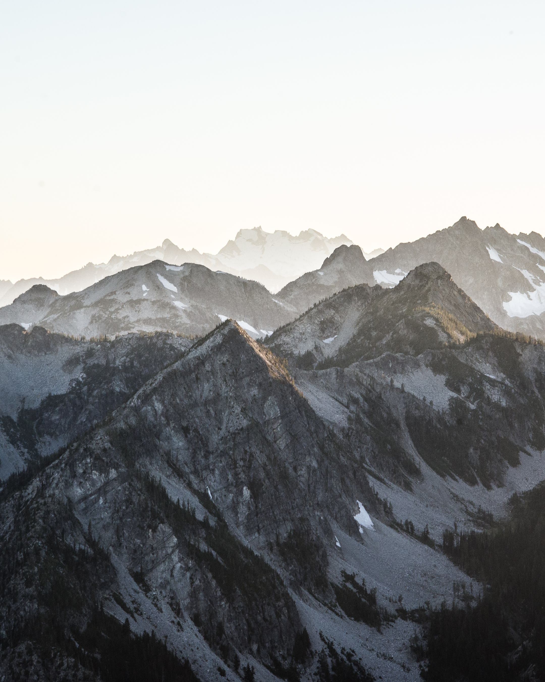 Berge in den Alpen bei Sonnenaufgang, mit Schnee auf den Gipfeln und dunklen Tälern.