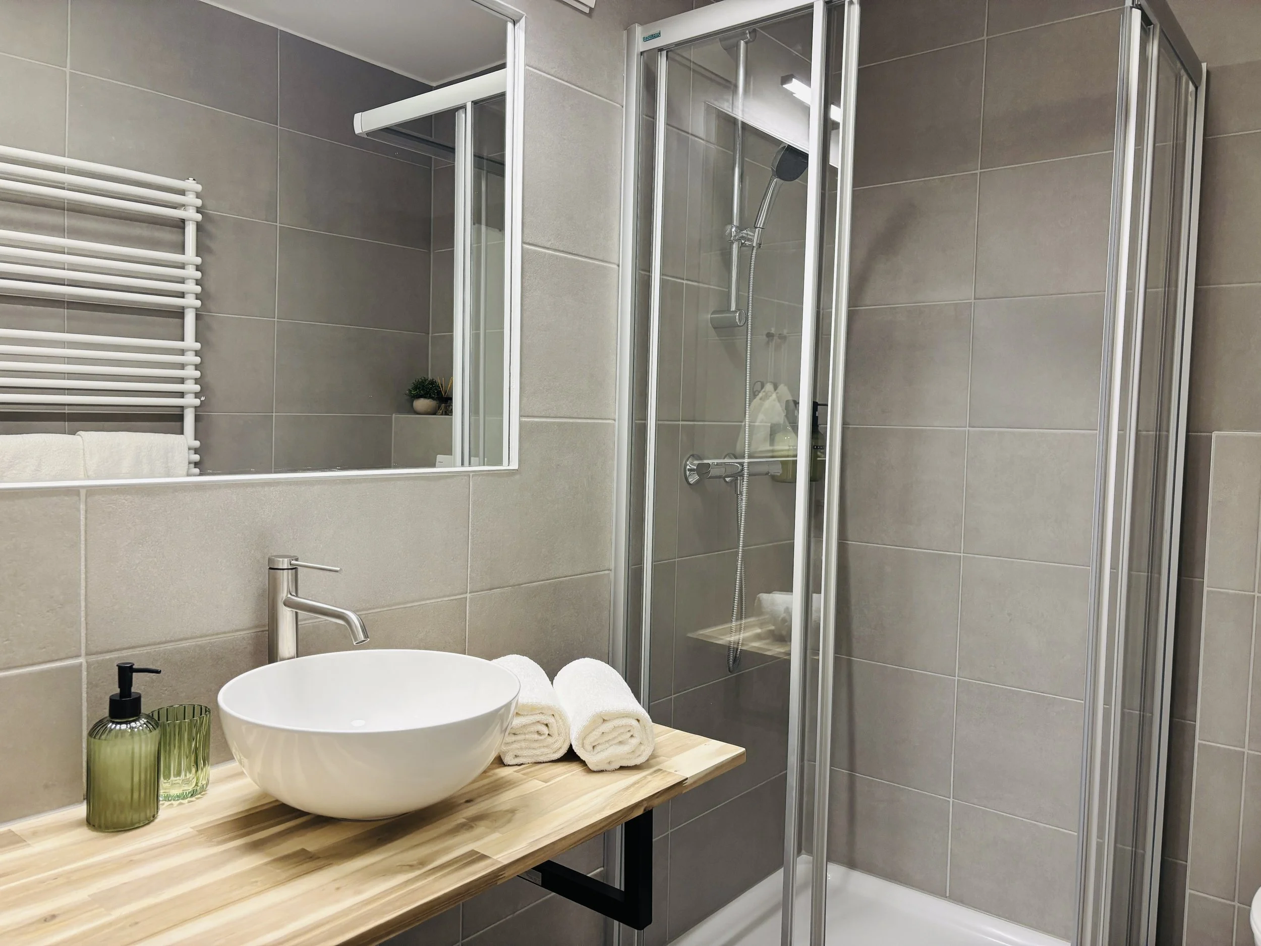 Moderner Badezimmerbereich mit Waschtisch, großen Spiegel, Handtüchern und einer Dusche mit Glaswand