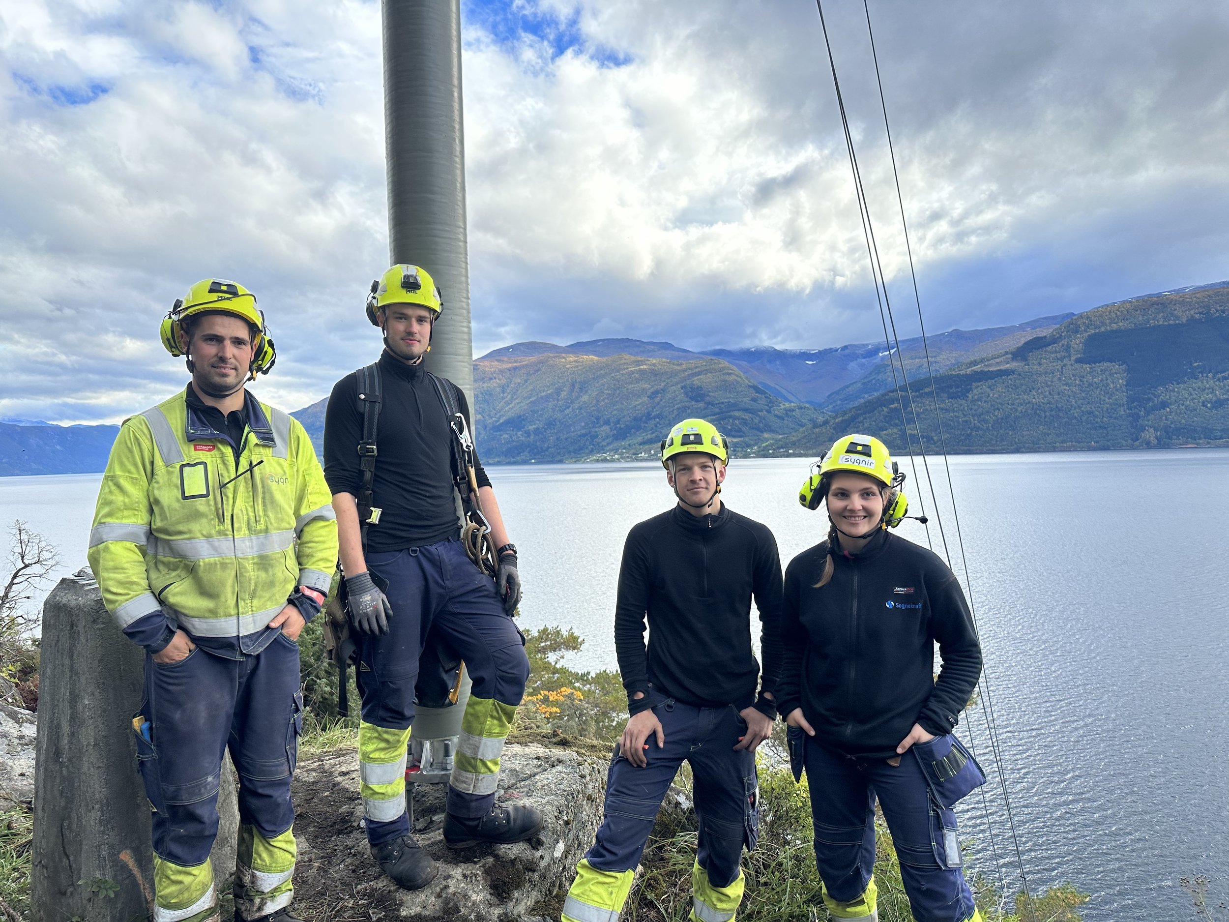 Fire smilande montørar med fjord og fjell i bakgrunn