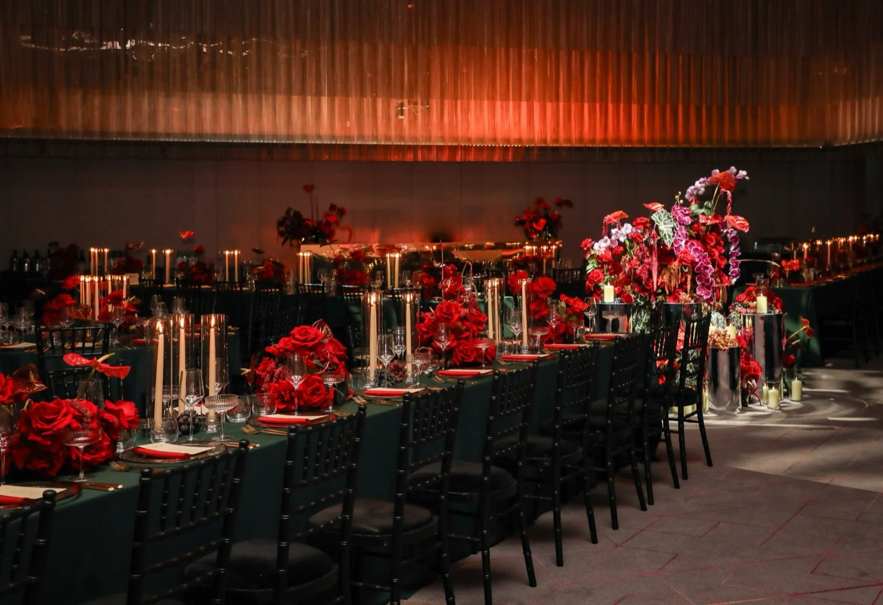 Elegant banquet table decorated with red flowers and tall candles in a dimly lit space, possibly for a wedding or formal event.