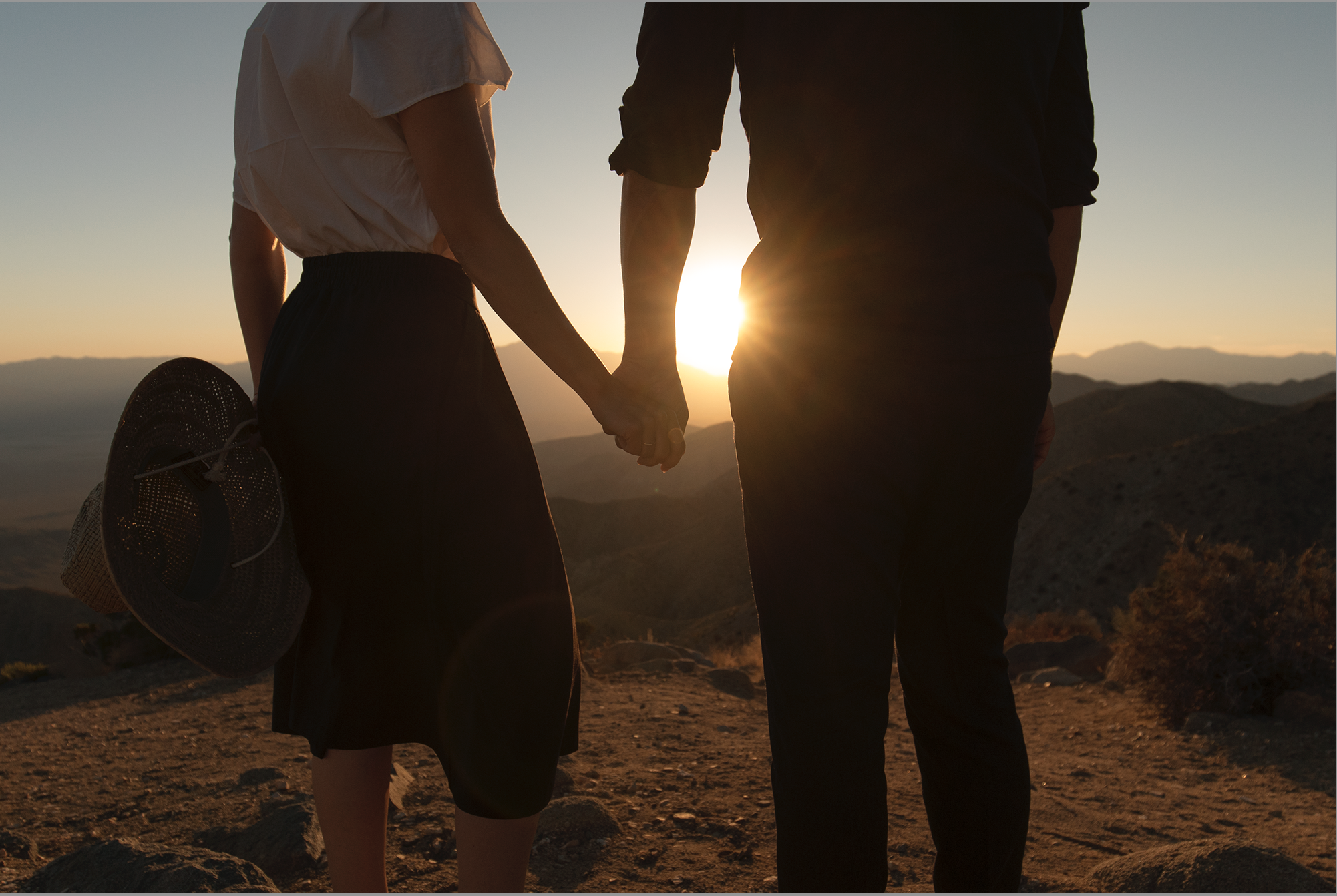 Couple holding hands during sunset in a desert landscape.