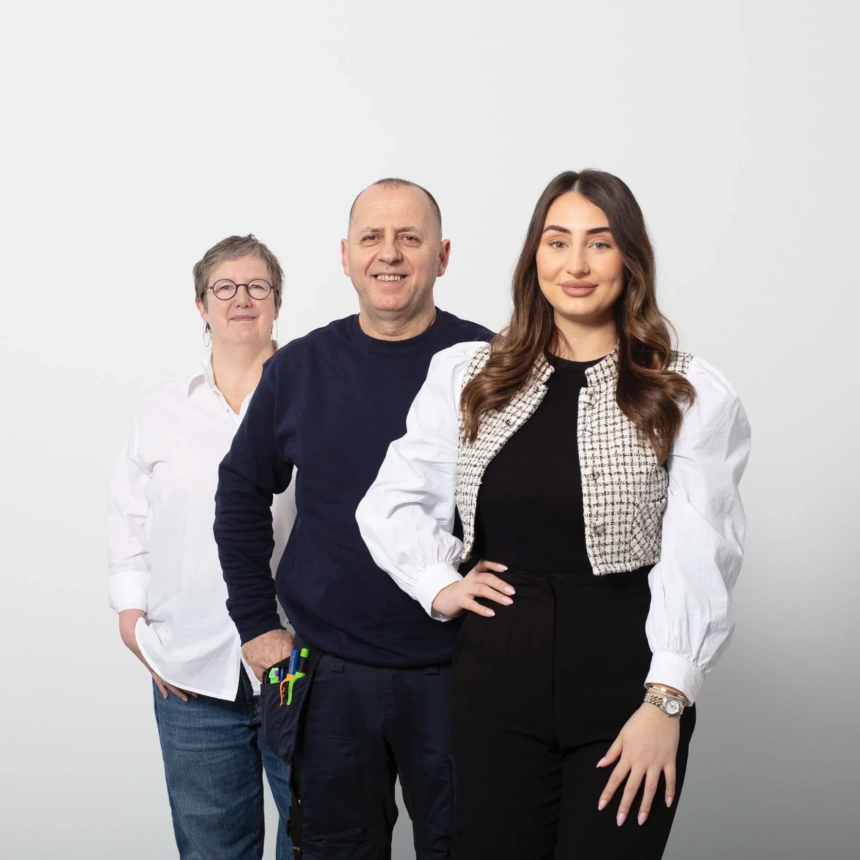 Group portrait of three people standing in a row against a plain white background, with the woman in the front and center, a man in the middle behind her, and an older woman in the back to the left.