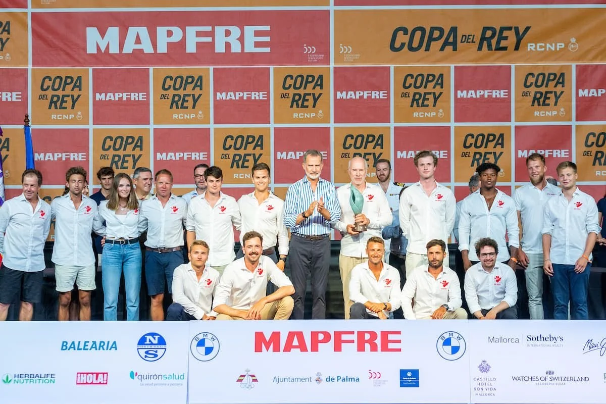 A group of men and women in white shirts posing on a stage with a large banner behind them that reads 'MAPFRE' and 'Copa del Rey'. Some individuals are holding a trophy.