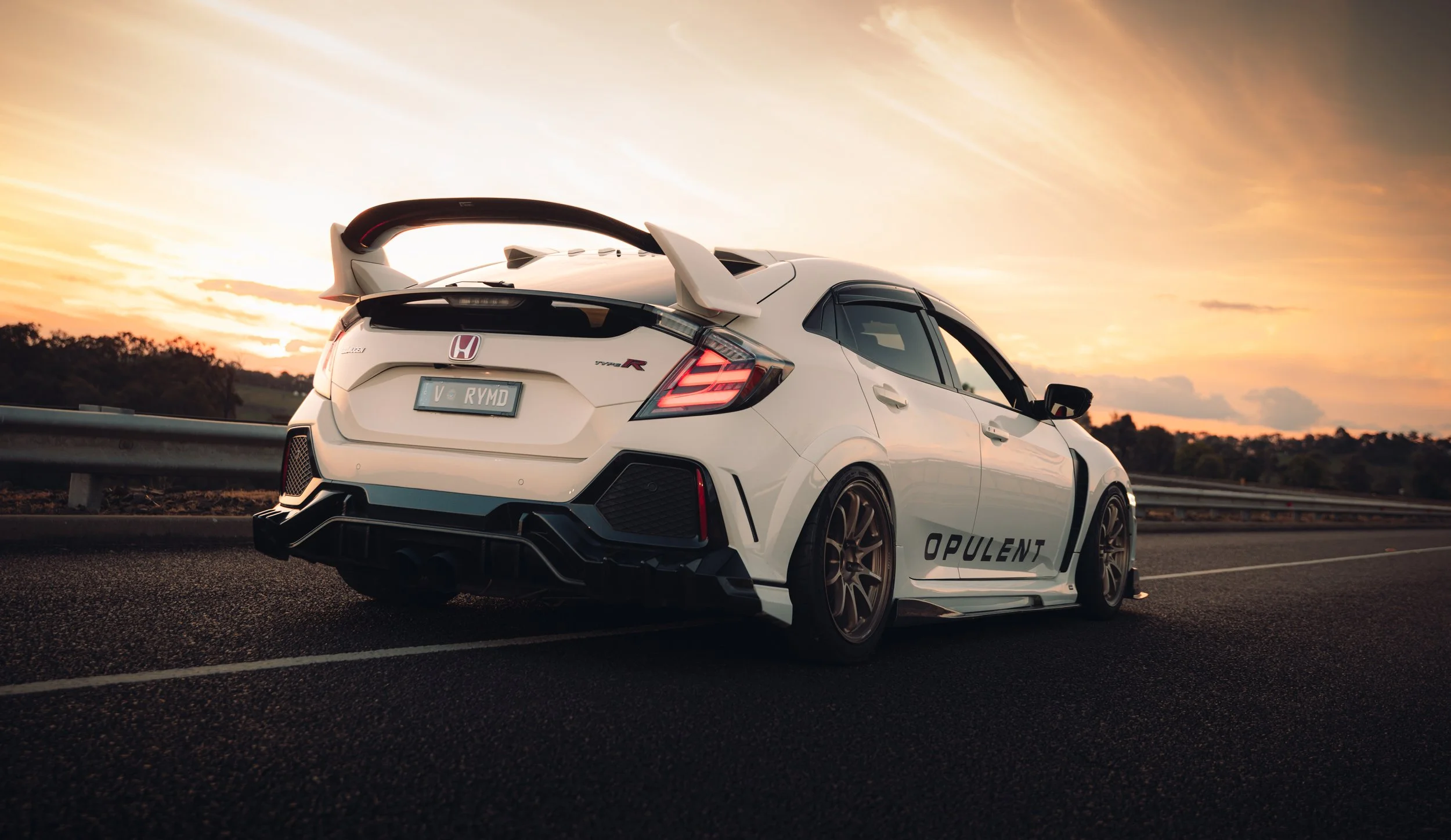 A white Honda Civic Type R with a large rear spoiler parked on the side of a highway during sunset.