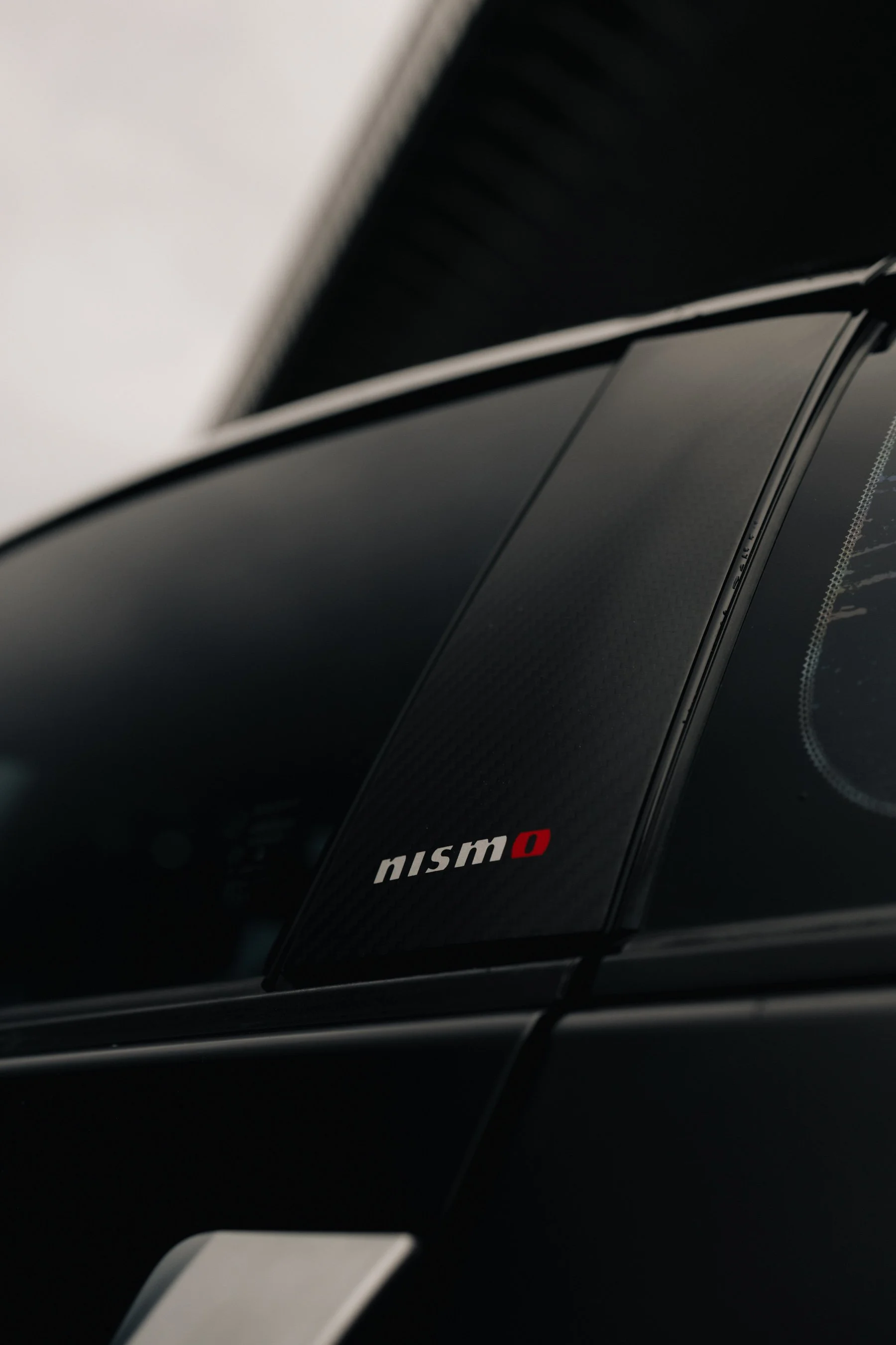 Close-up of a Nissan Nismo car badge on the vehicle's exterior, featuring black and red accents. Nissan 350Z, jdm, nissan photo, jdm car, work wheels, work photo, underground spot, lowered car. 