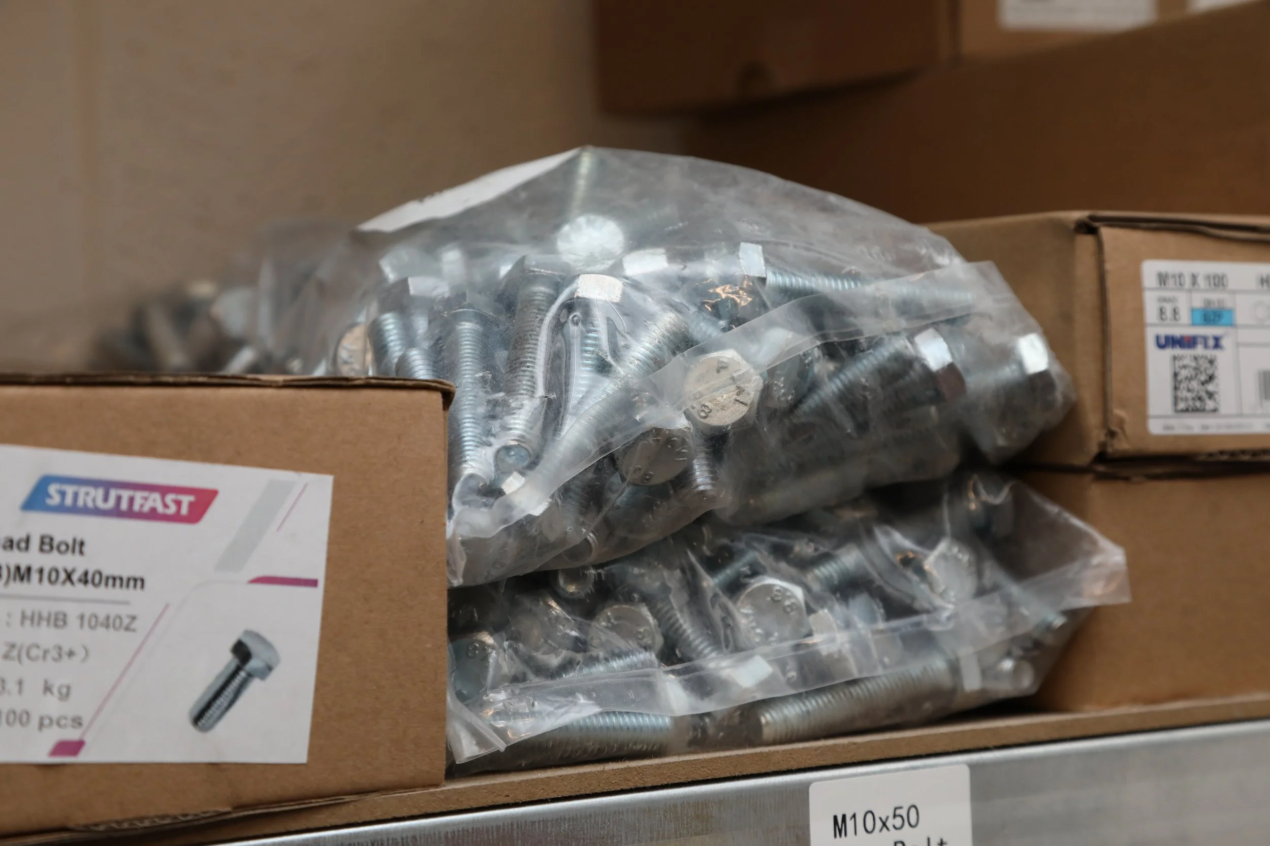 Plastic bag filled with silver bolts on a shelf next to boxes of hardware.