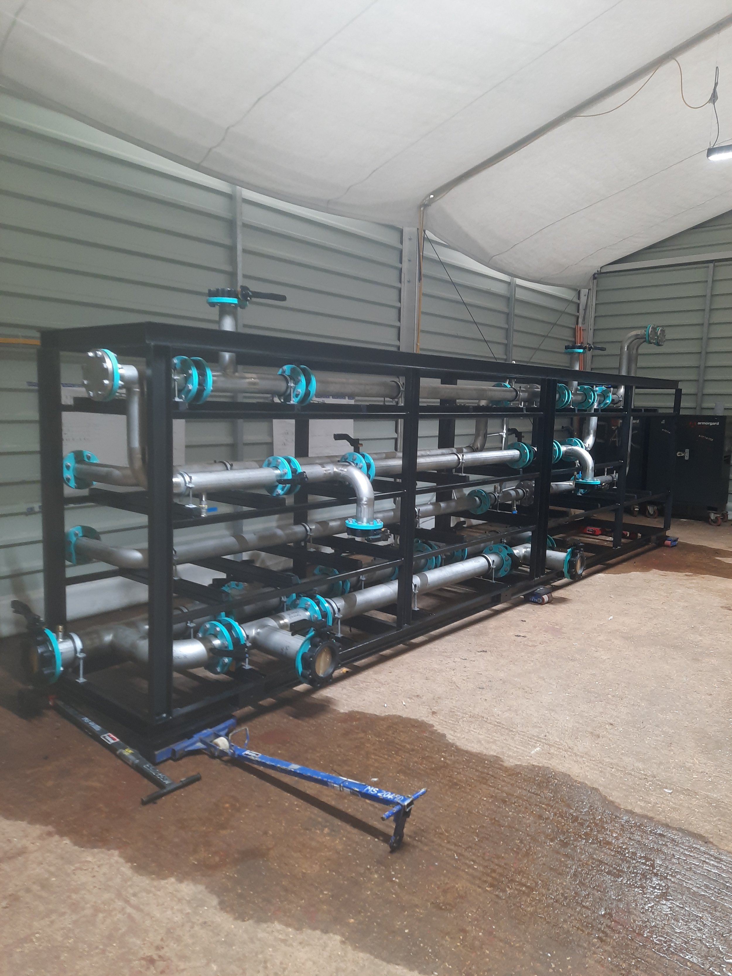 Industrial piping system with metal pipes, blue valve fittings, and a black metal framework inside a storage or maintenance area.