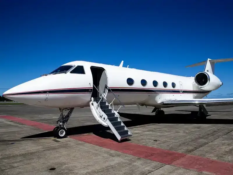 White private jet with open door and stairs on tarmac under blue sky.