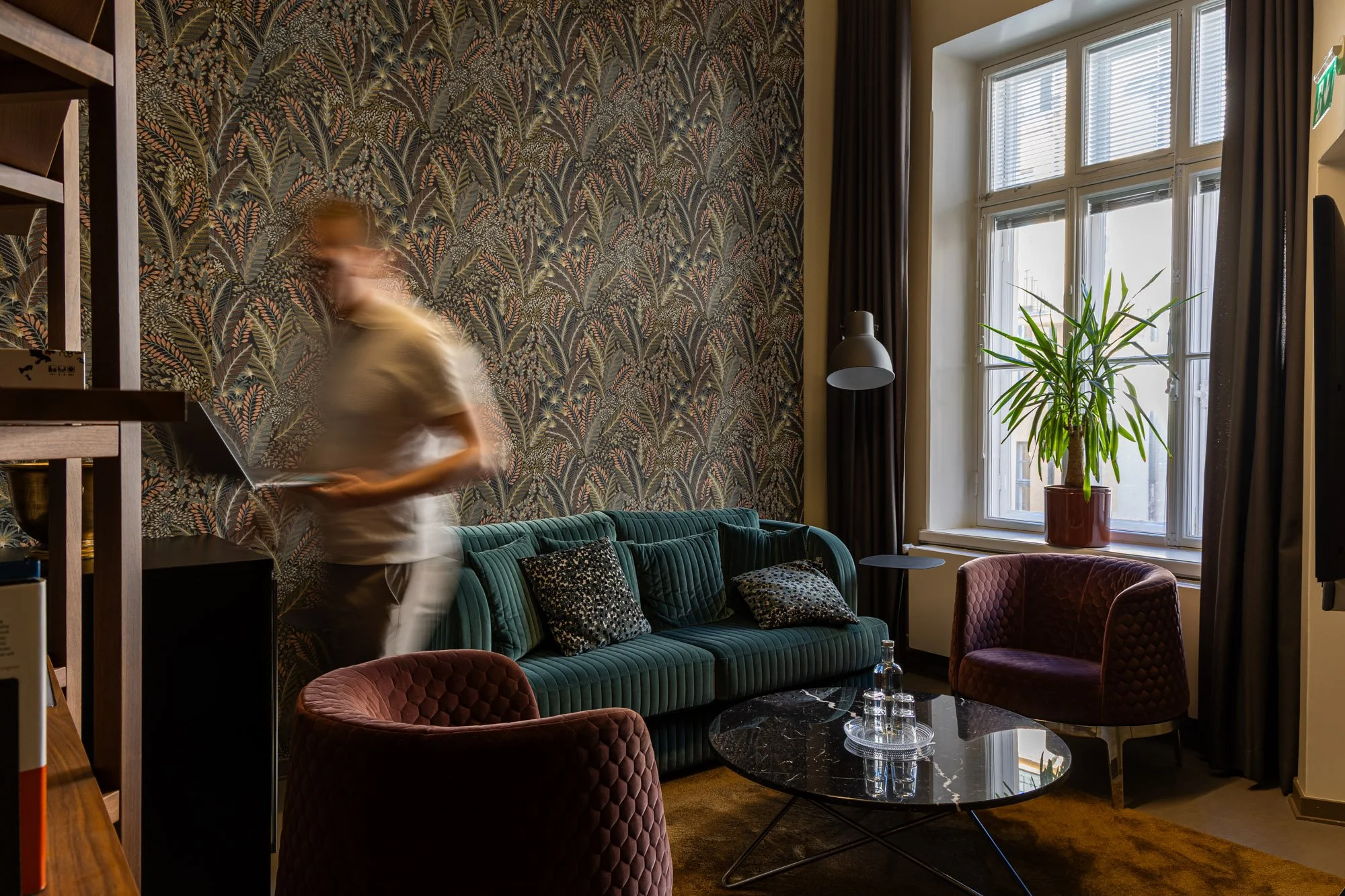 Sisäkuva viihtyisästä toimistotilasta, jossa on tummanvihreä samettisohva ja musta marmoriallaspöytä. Iso ikkuna valon tulvii huoneeseen, ja ikkunalaudalla on iso vihreä kasvi. 