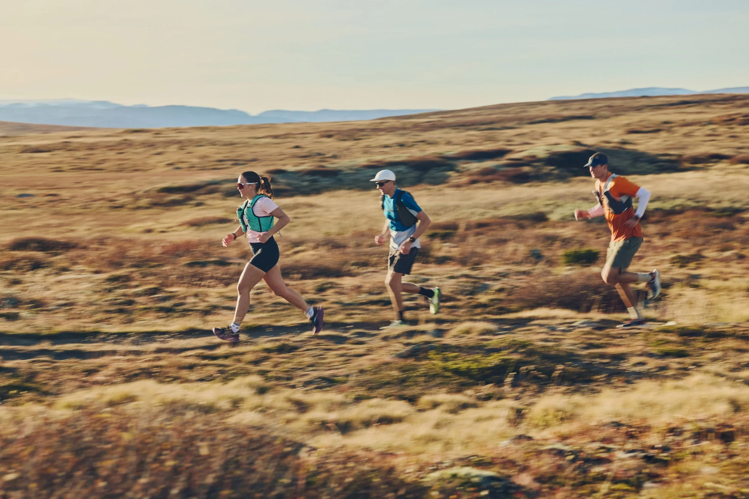 Three people trail running through a grassy, open landscape with mountains in the background during the day at Geilo - Geilo Trail Run / GTR
