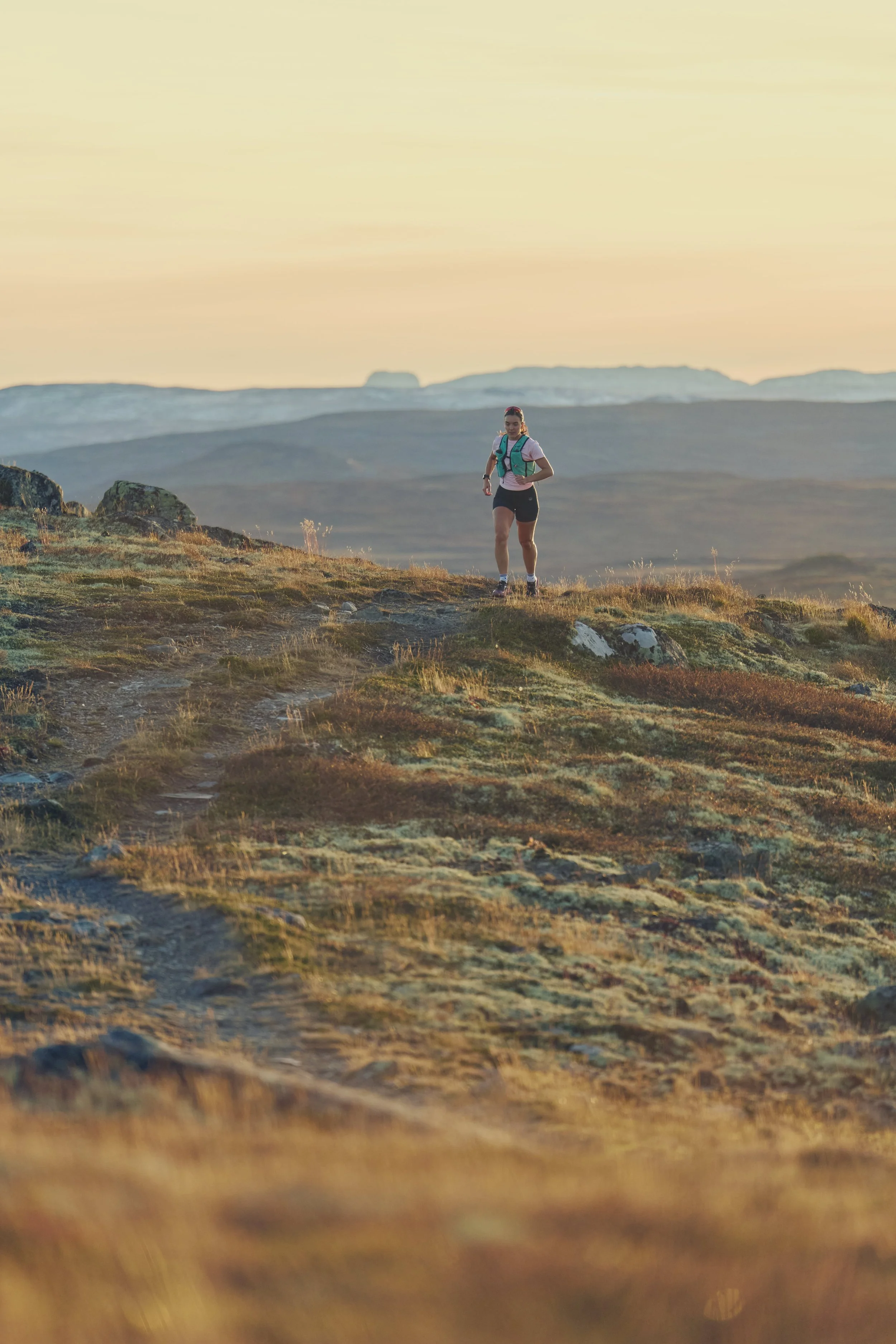A woman hiking on a trail in a mountainous landscape during sunset.