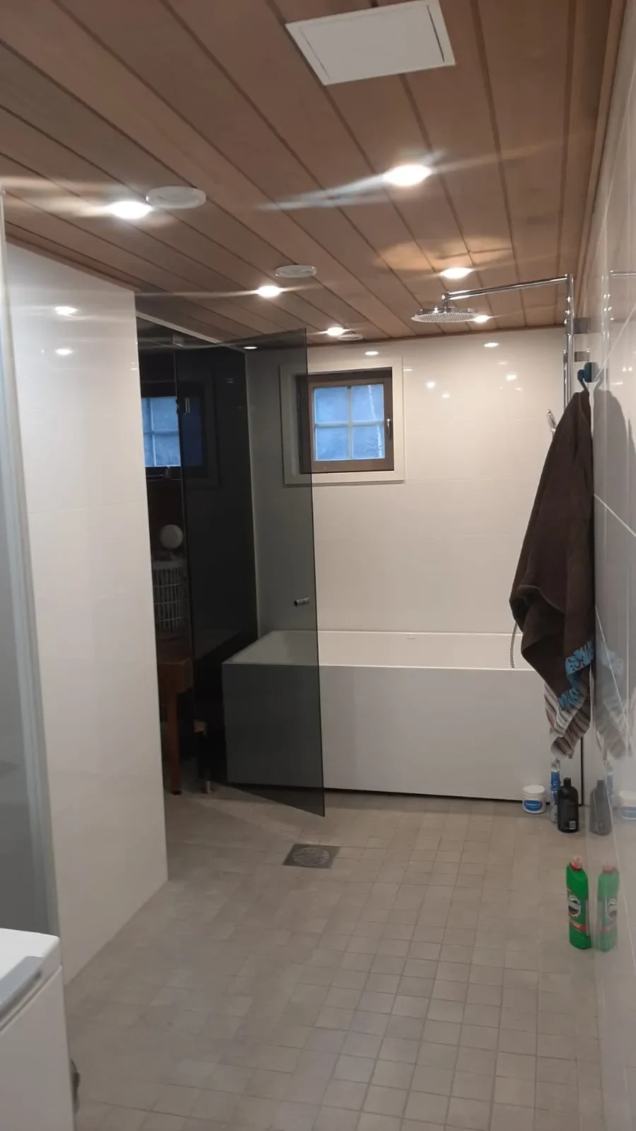 Kuva kylpyhuoneesta, jossa on valkoinen kylpyamme, pieni ikkuna ja hanalla varustettu pyyhe koukku.