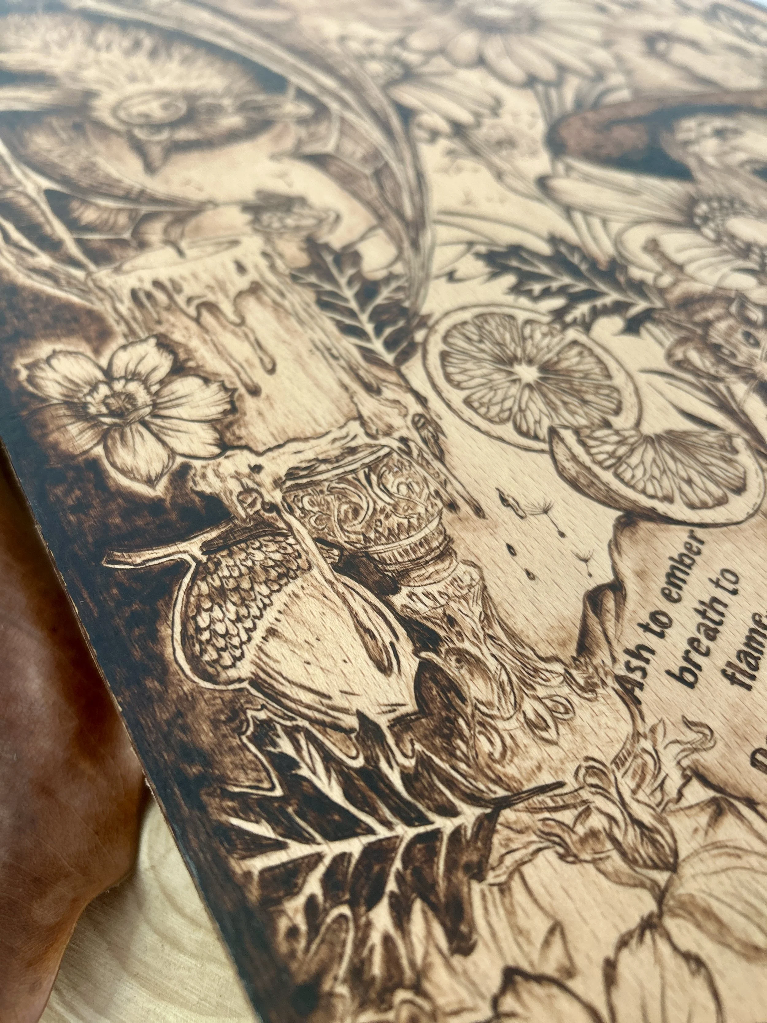 Macro view of pyrography details showing a dried orange slice, leaves, and floral patterns burned into a light wood surface.