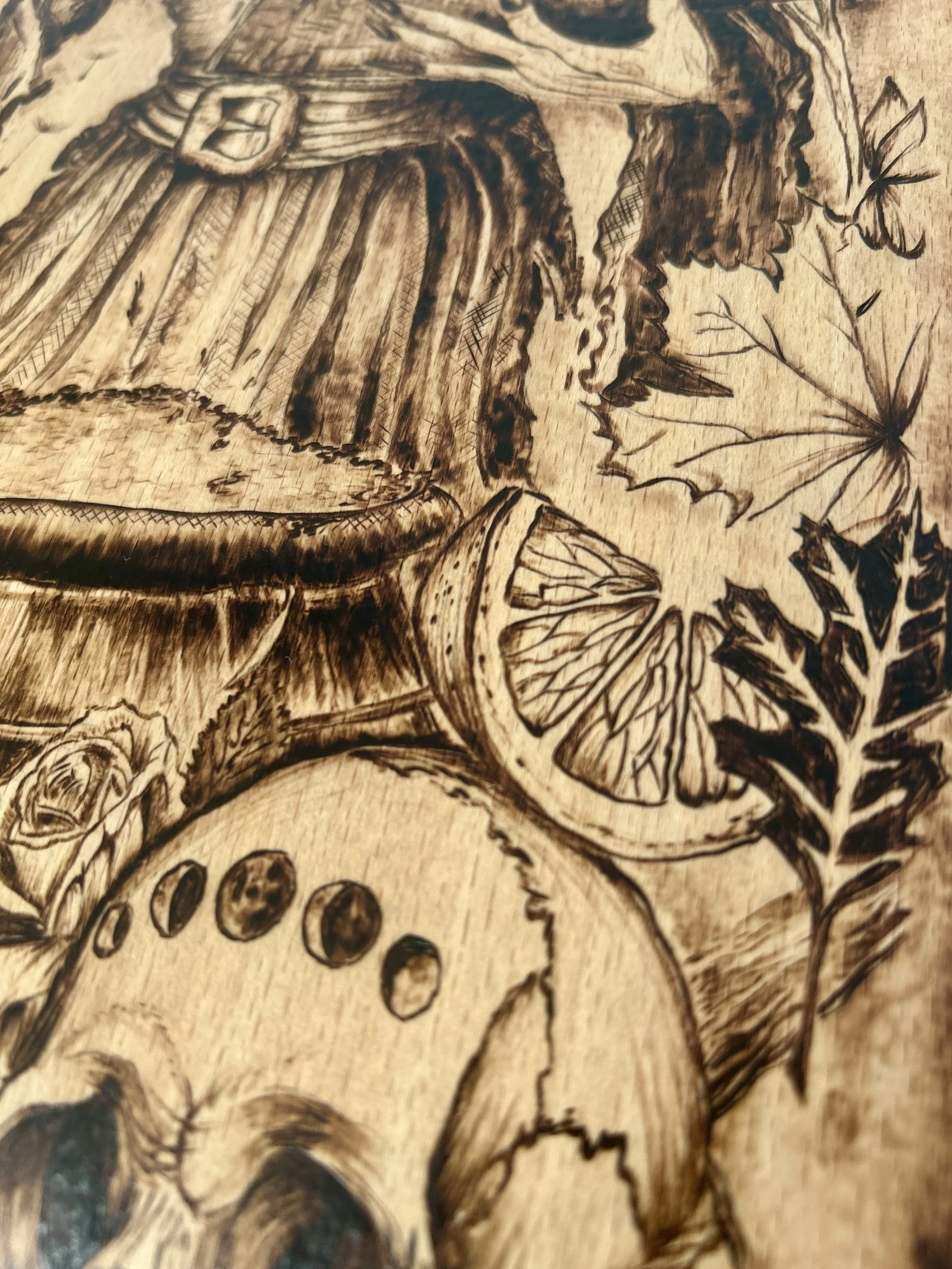 Close-up of botanical and occult elements, including a cauldron rim, dried citrus, and autumn leaves burned into the wood.