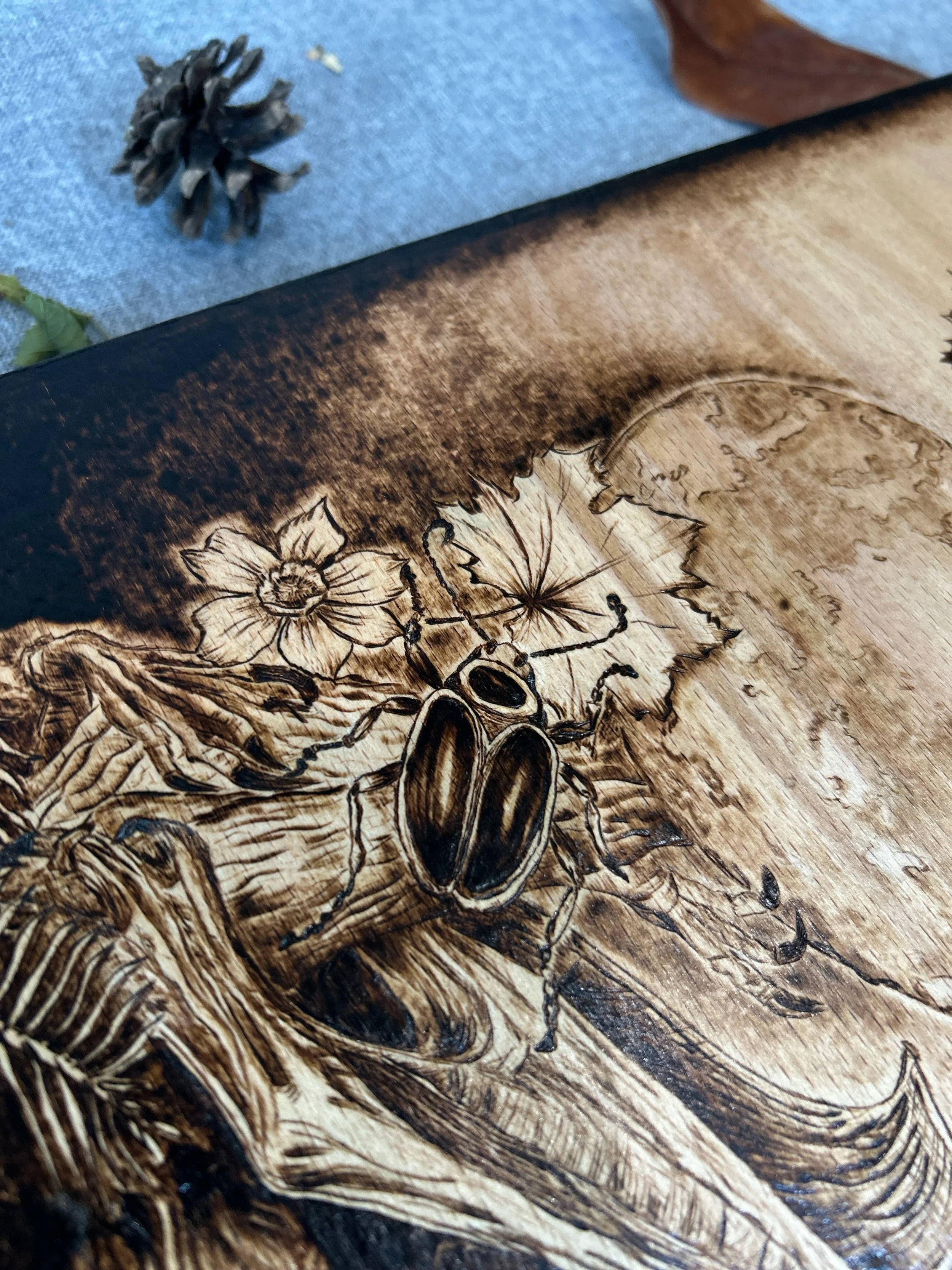 Extreme close-up of tiny insect antennae and daisy petals in The Darkest Wishes pyrography, demonstrating artisanal fire craft precision."