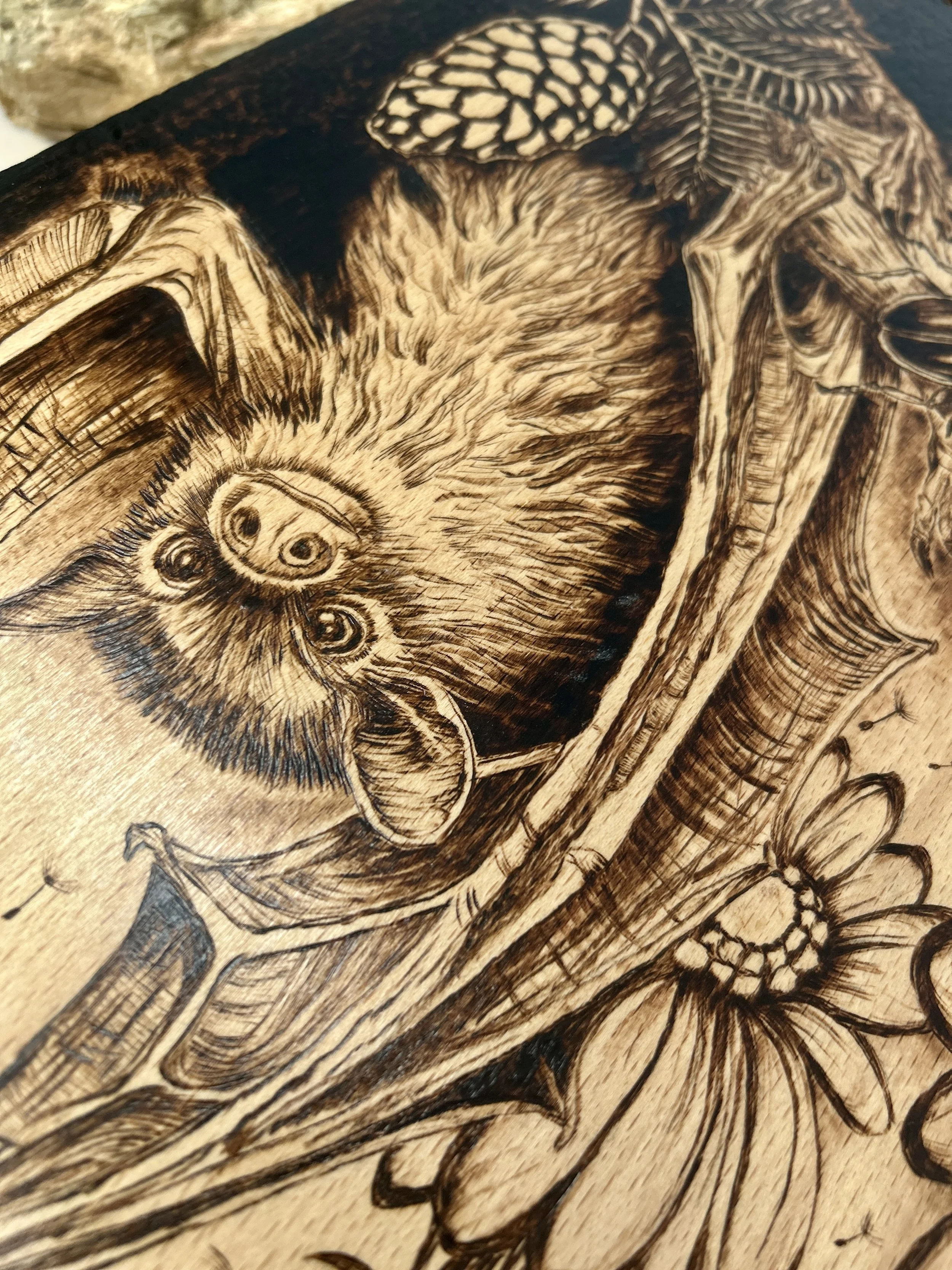 Central focus on the wood-burned bat, capturing the realistic fur detail and the bat’s facial features hanging from a branch.