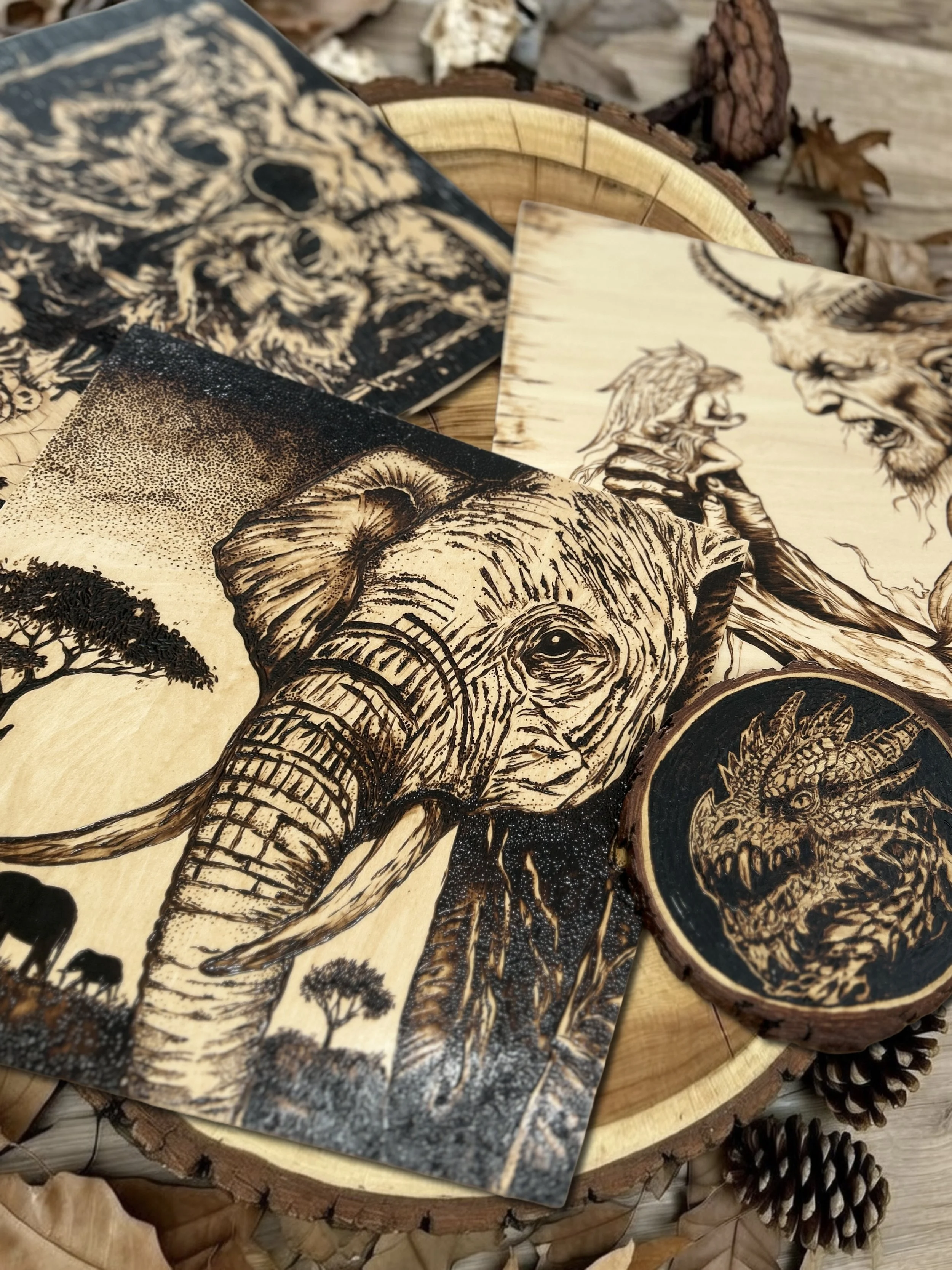 Collection of detailed wood-burned pyrography artworks on natural wood, featuring an elephant, a dragon, a wolf, wood-burning decor