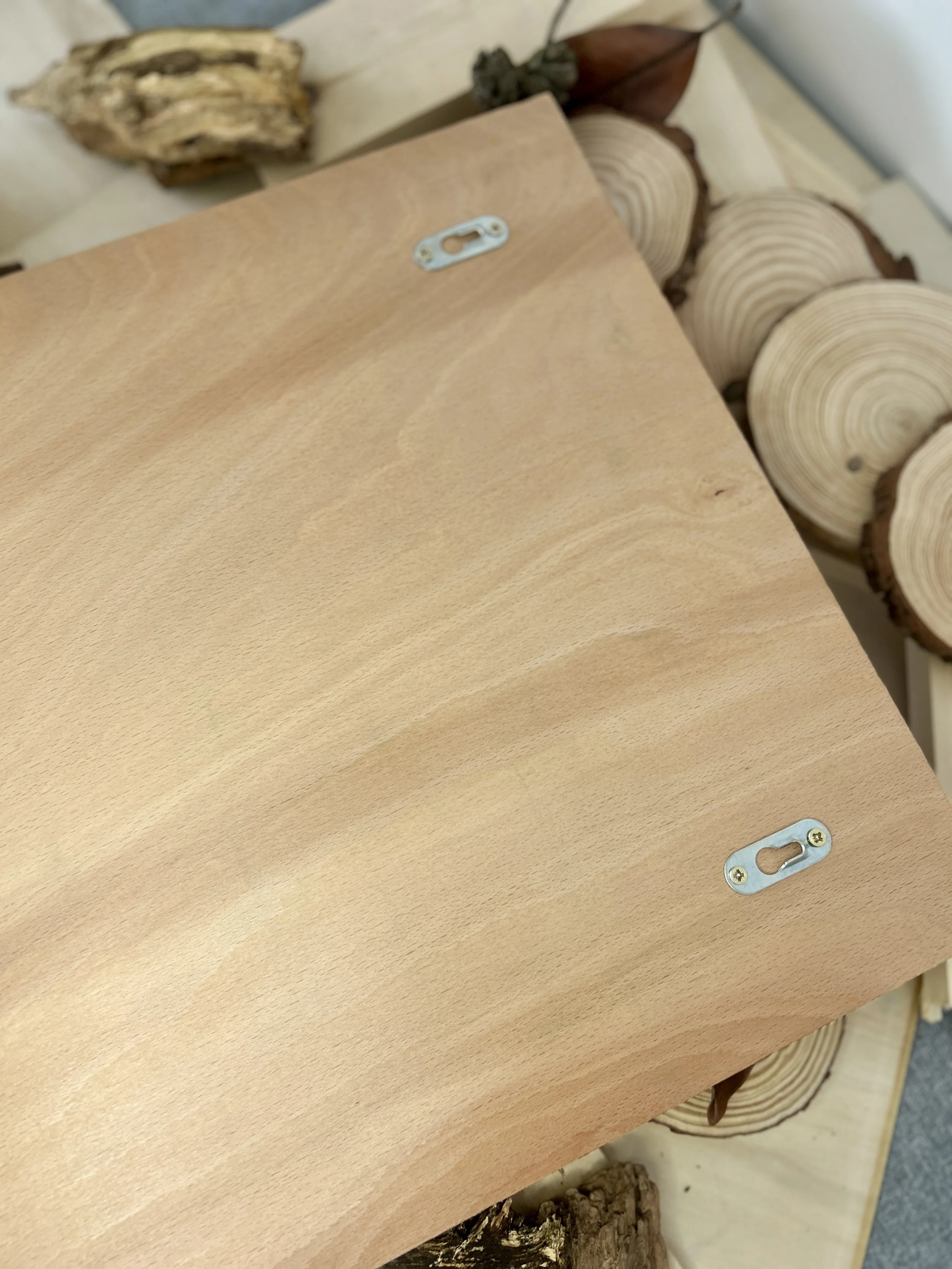 View of the back of the wooden art piece, showing the clean natural wood grain and two silver metal saw-tooth hangers for wall mounting.