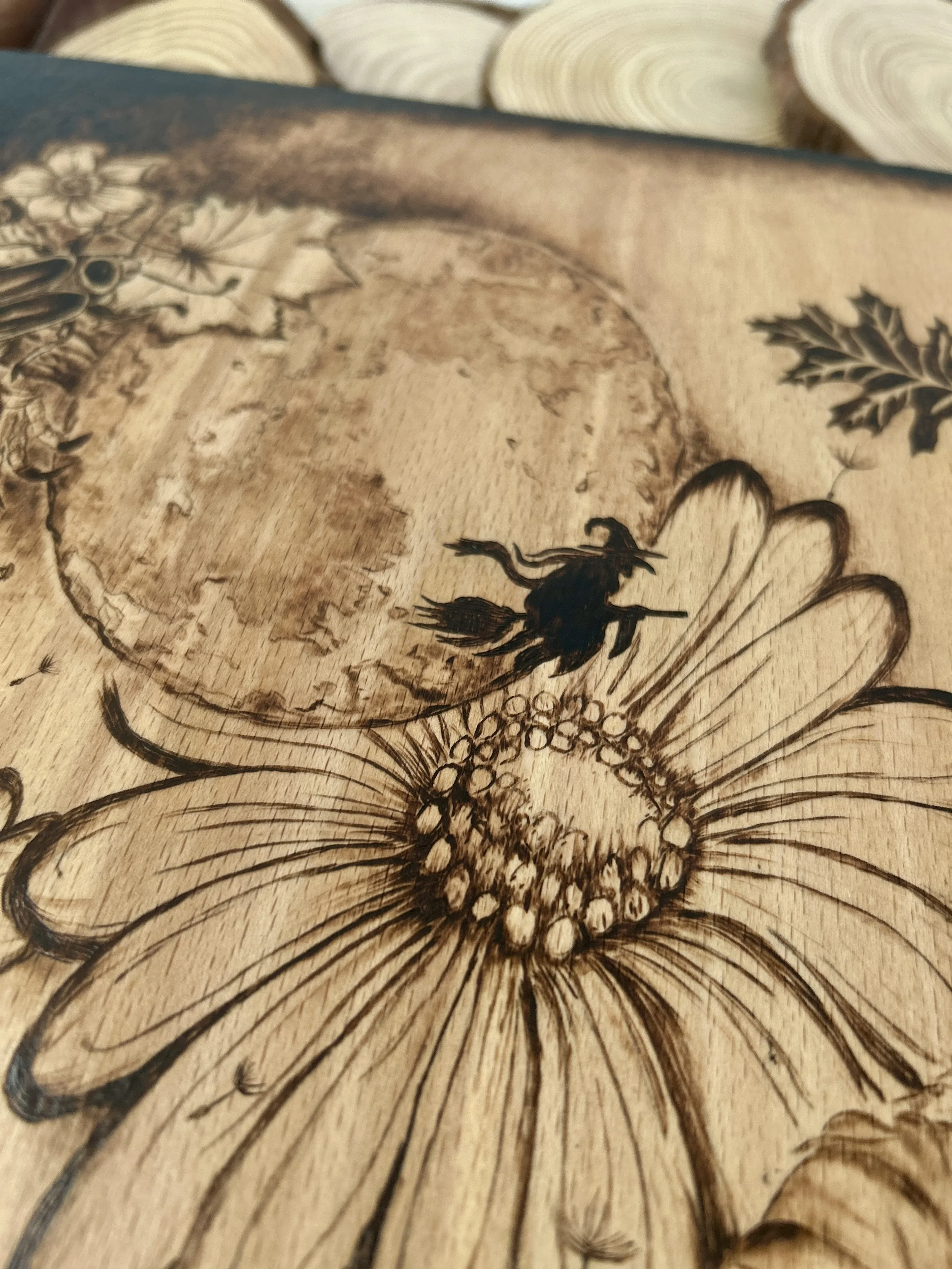 Close-up of a full moon and a tiny witch silhouette flying on a broomstick, surrounded by large sunflowers in pyrography.