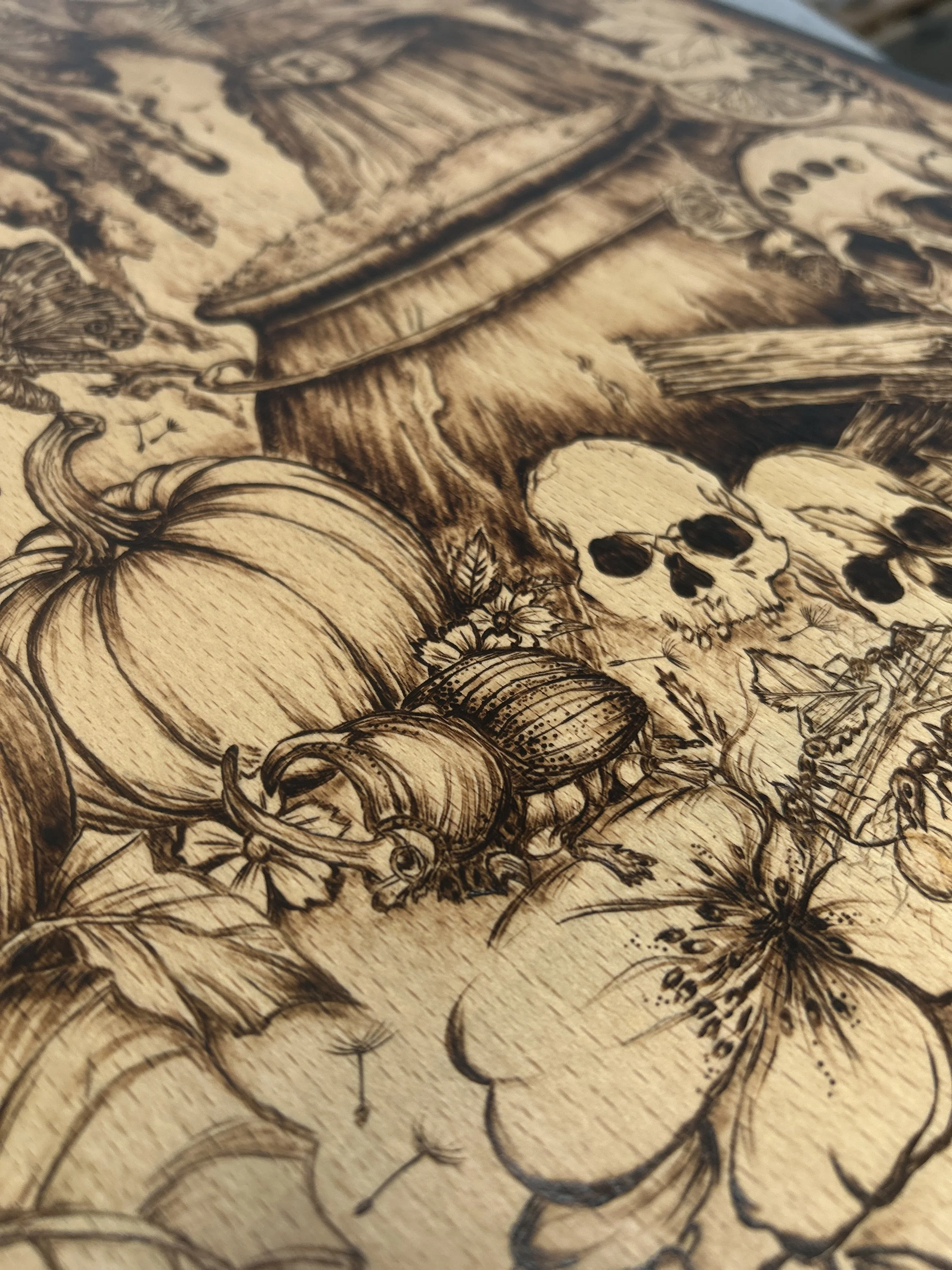 Close-up of the bottom corner of the art, showing a large pumpkin next to a steaming wood-burned cauldron and small skulls.