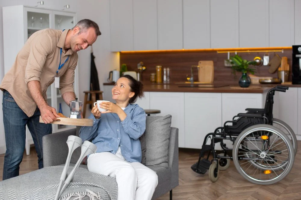 Man serving coffee to woman sitting on couch with crutches nearby in a modern kitchen