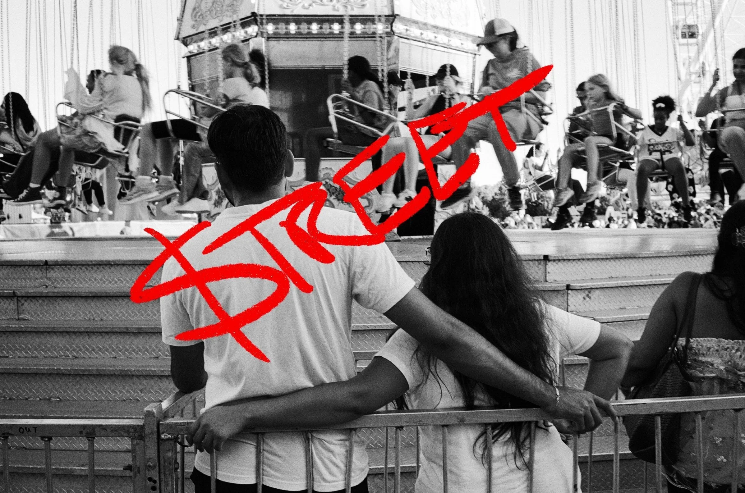 People sitting on a bench at a carnival or fairground watching a ride with children on spinning swings.