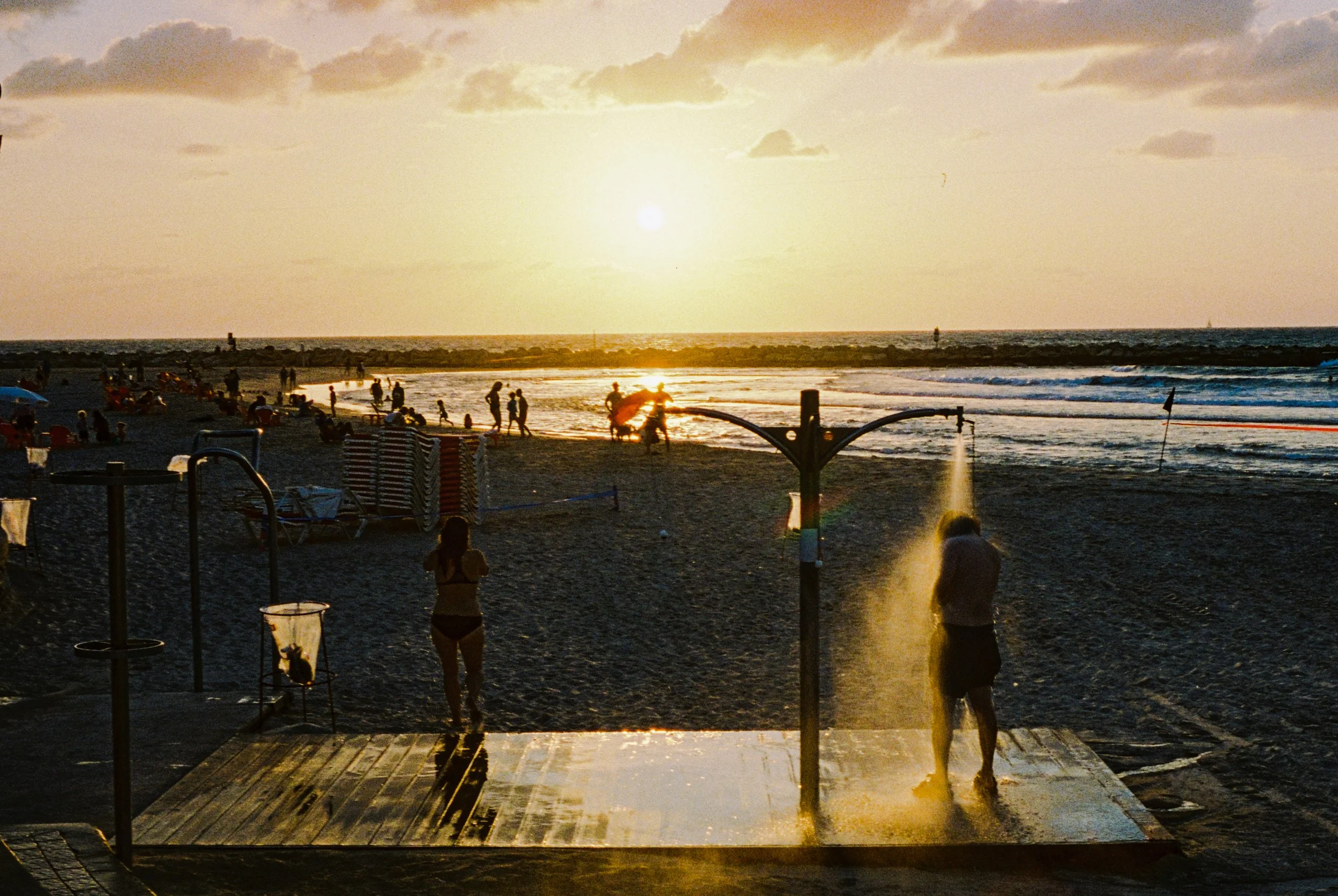 People enjoying shower on a beach at sunset with the ocean in the background and clouds in the sky.