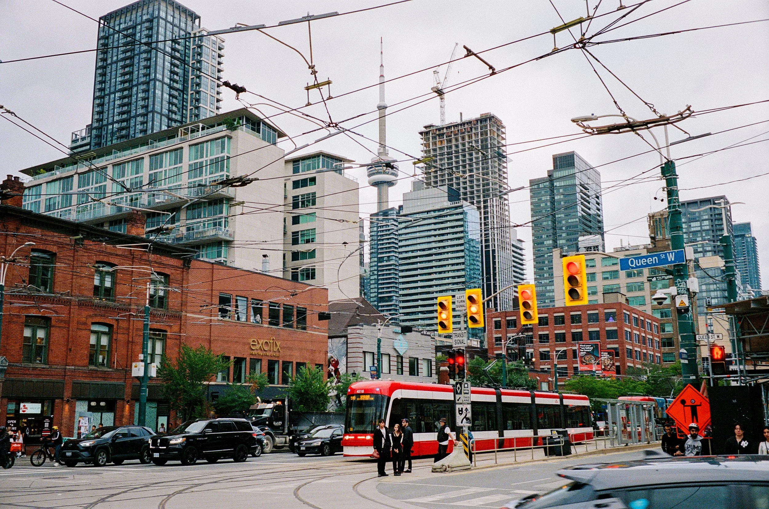 City street scene with tram, cars, pedestrians, and high-rise buildings in the background, including the CN Tower.