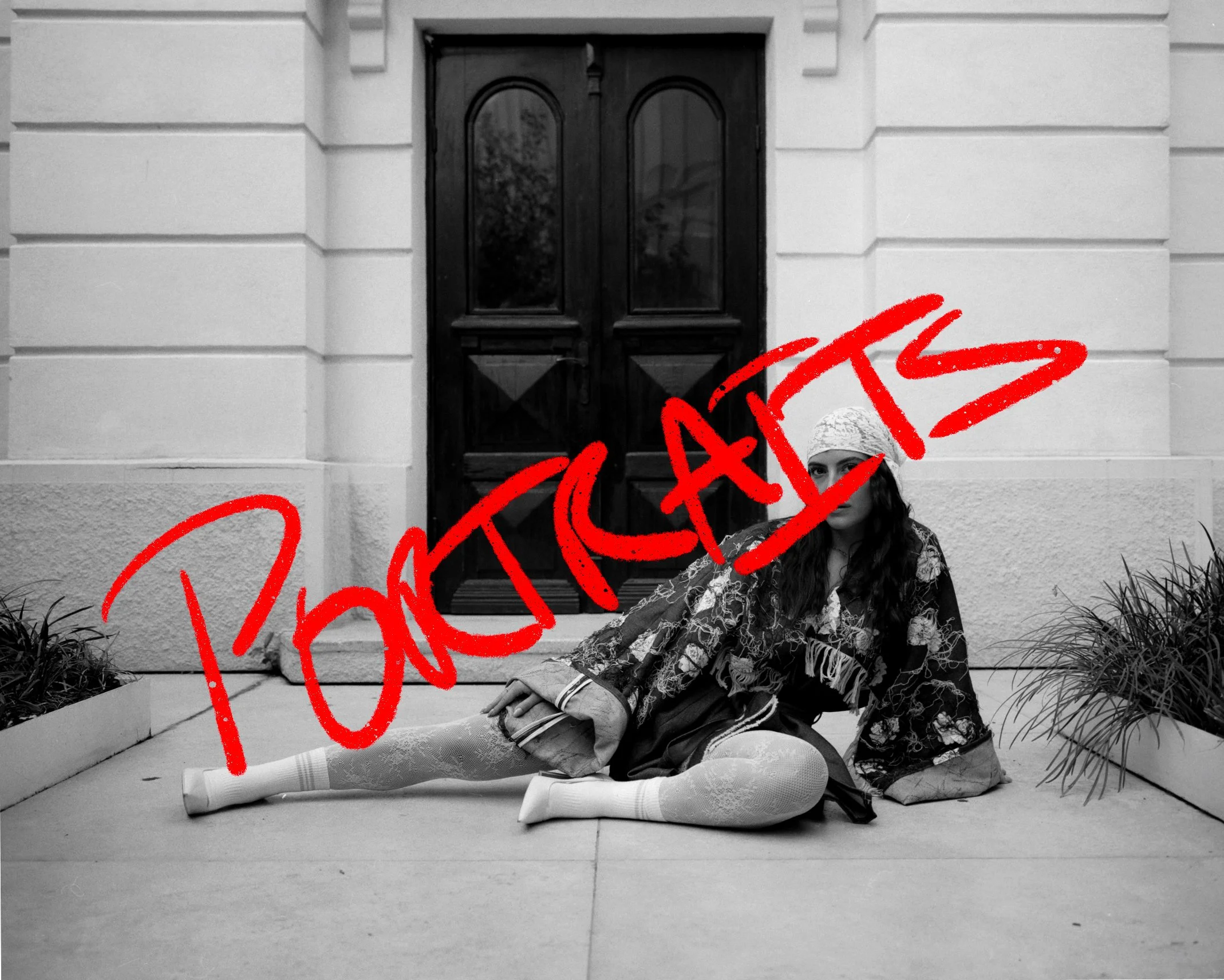 A woman with long curly hair wearing a patterned coat, lace skirt, and white socks and shoes, sitting on the ground outside a building with a wooden door. The image is in black and white with the word "PHOTOGRAPHY" written in bold red across the image.