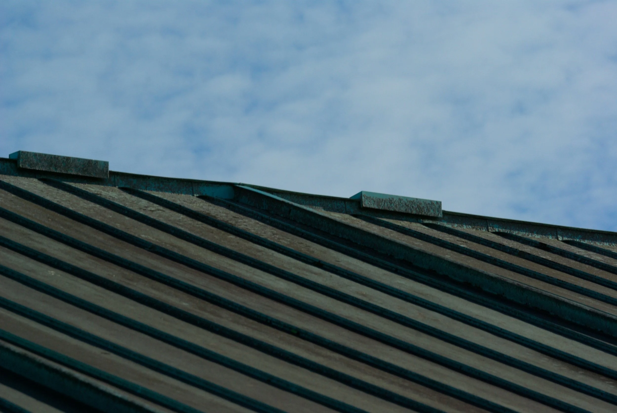 Close-up of a rooftop with greenish metal panels and a cloudy blue sky in the background.