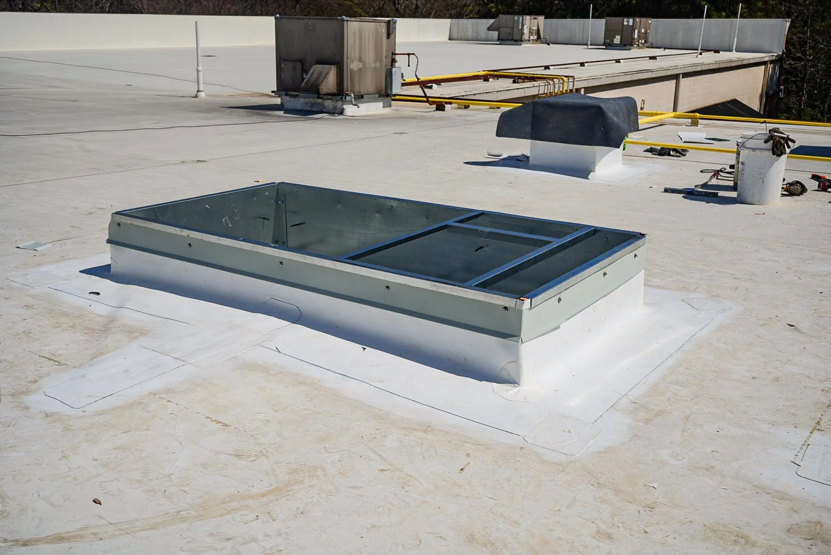 A rooftop with a skylight, surrounding fenced area, and various rooftop equipment and tools.