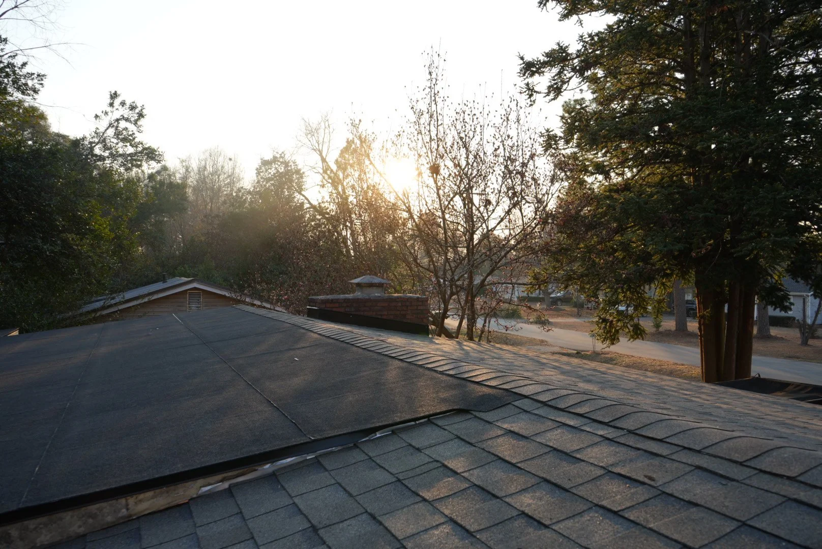 Sunset or sunrise view from a house roof with trees and neighborhood street in the background.
