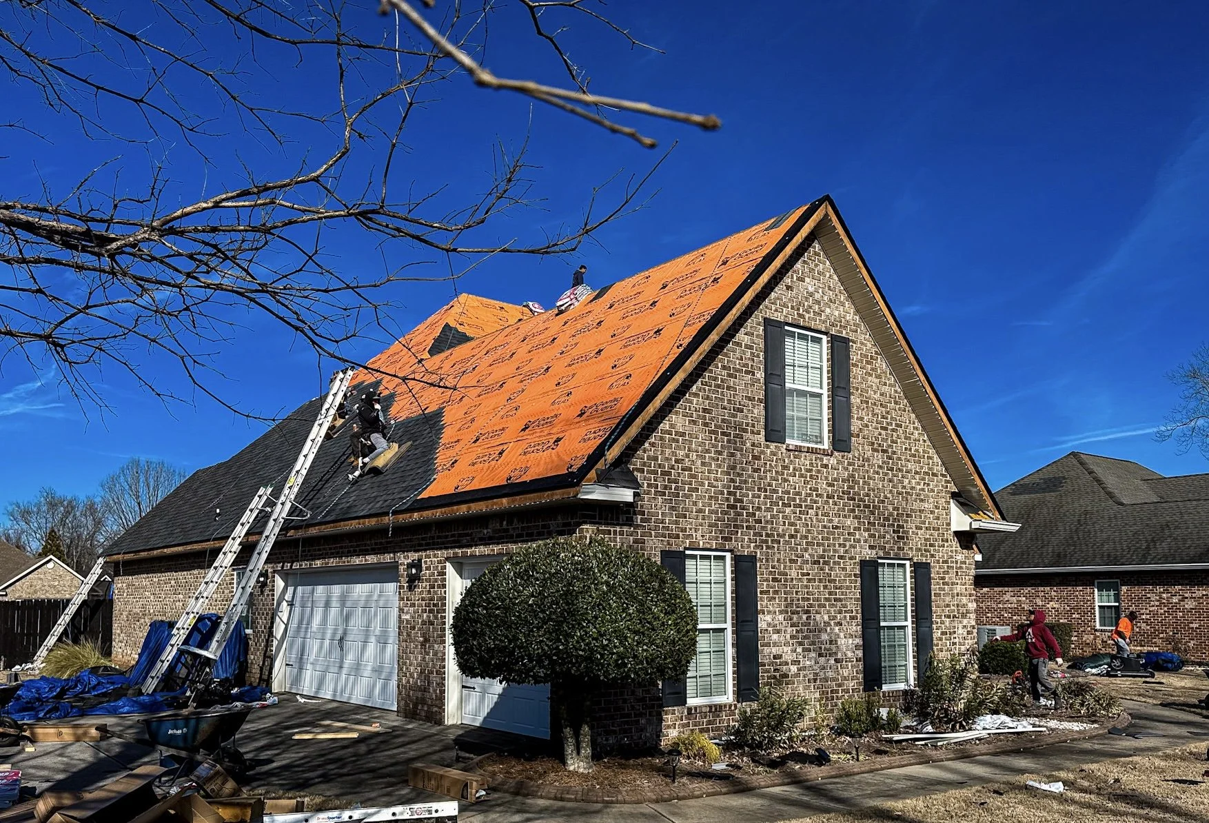 Workers installing new asphalt shingles on the roof of a brick house during daytime.