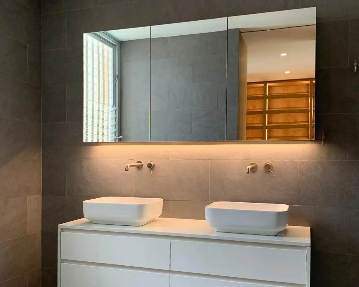 Modern bathroom with two vessel sinks on a white vanity, wall-mounted faucets, a large mirror, and a window with a blind.